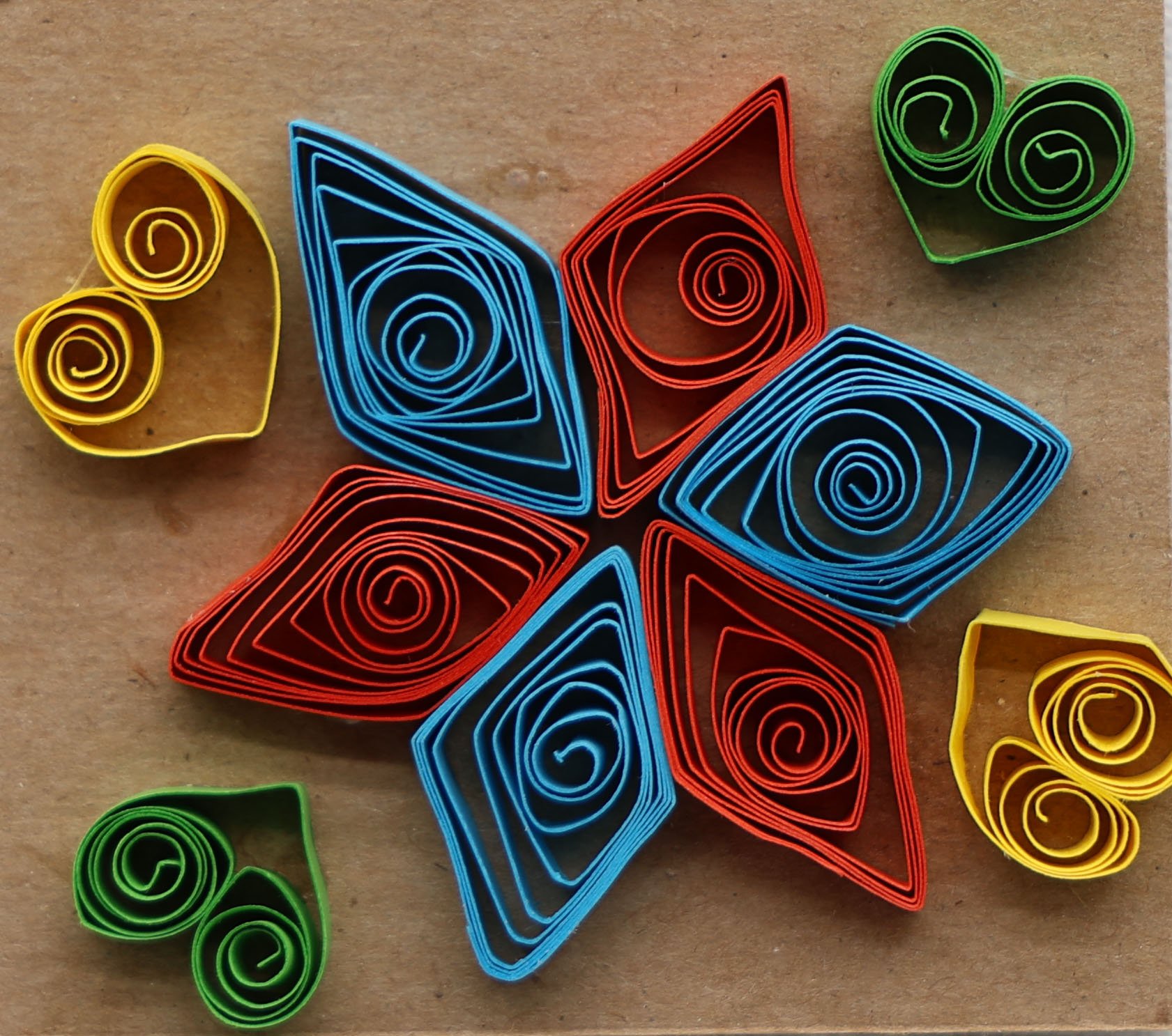 Colorful quilled paper leaf-shaped and heart-shaped designs arranged in a star shape on a brown background.