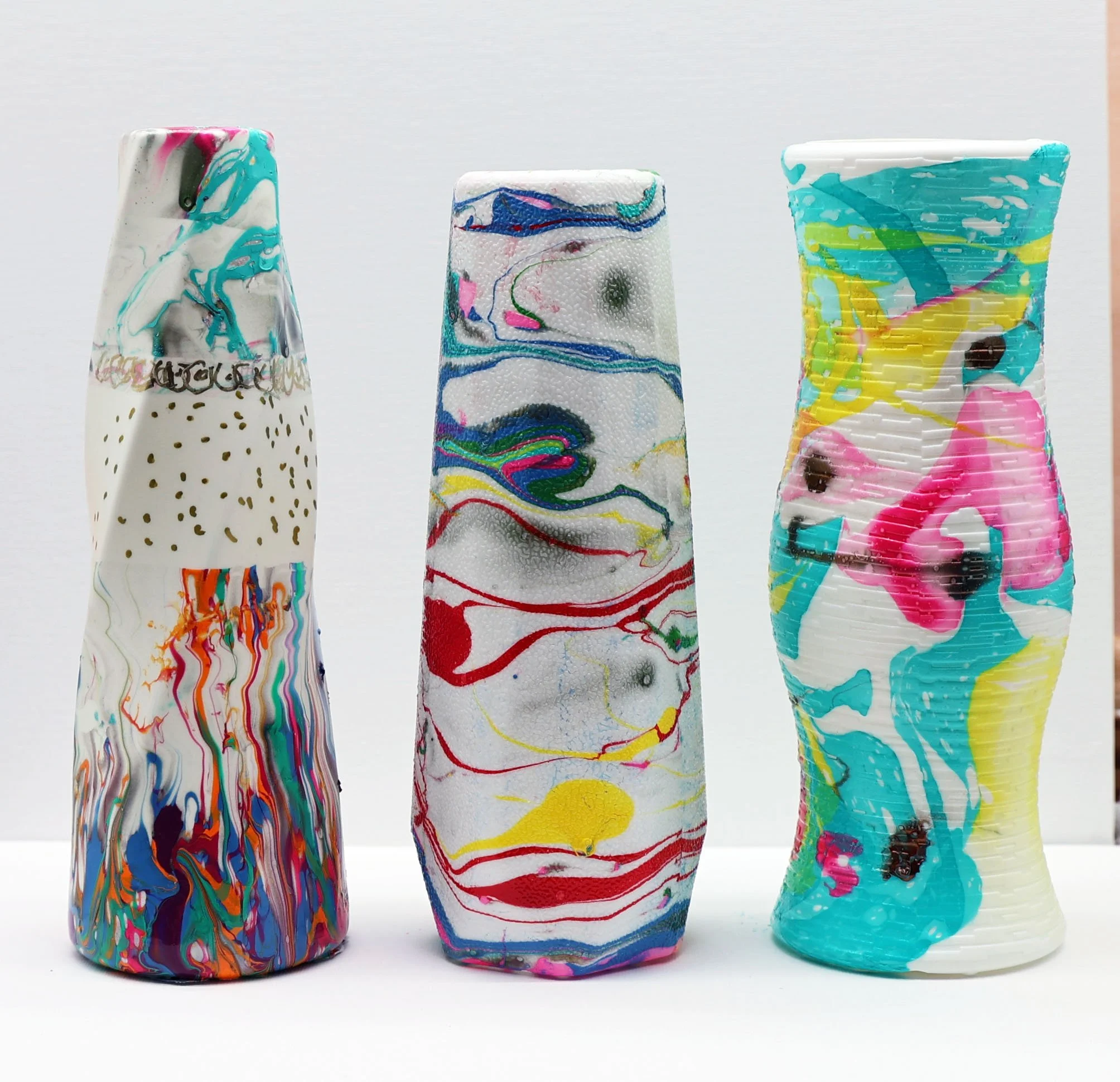 Three colorful, abstractly painted glass vases with swirling patterns, placed side by side on a white surface.