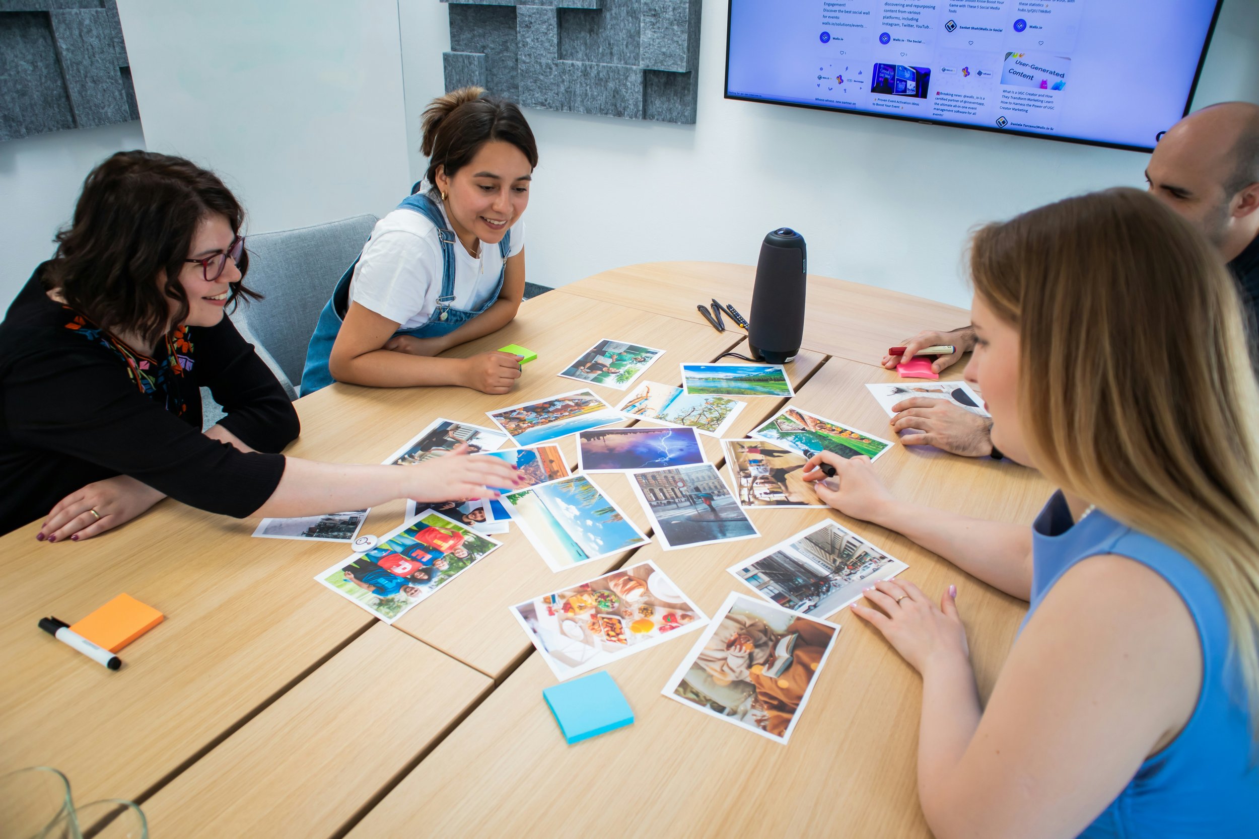 Four people sitting around a wooden conference table with printed photos spread out, discussing and sharing ideas in a modern office conference room.