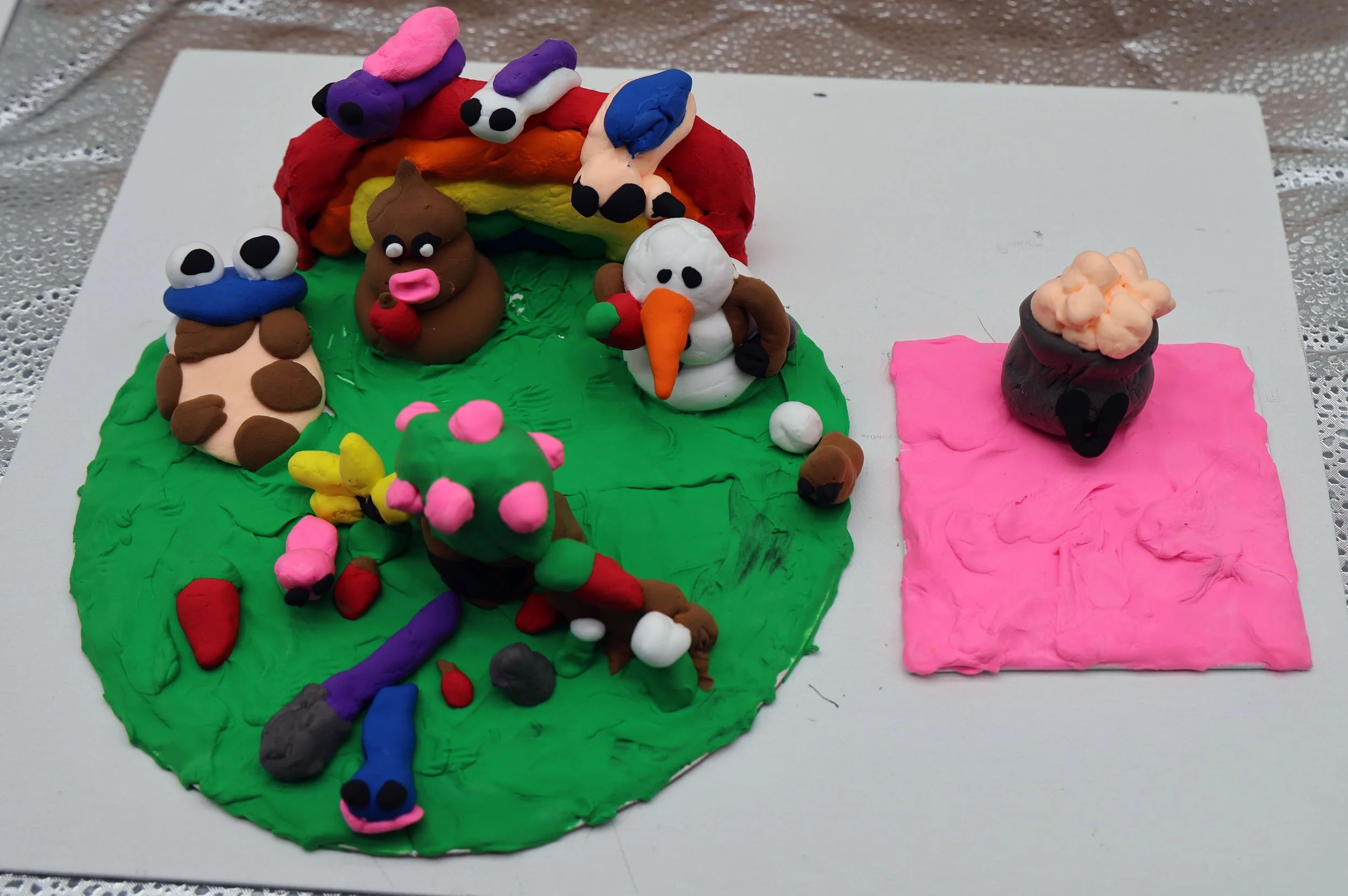 Colorful clay model depicting characters from the Super Mario game, including a rainbow, a brown character with a pink nose, a snowman with a carrot nose holding an apple, a smaller green character with pink spots, and various other whimsical figures