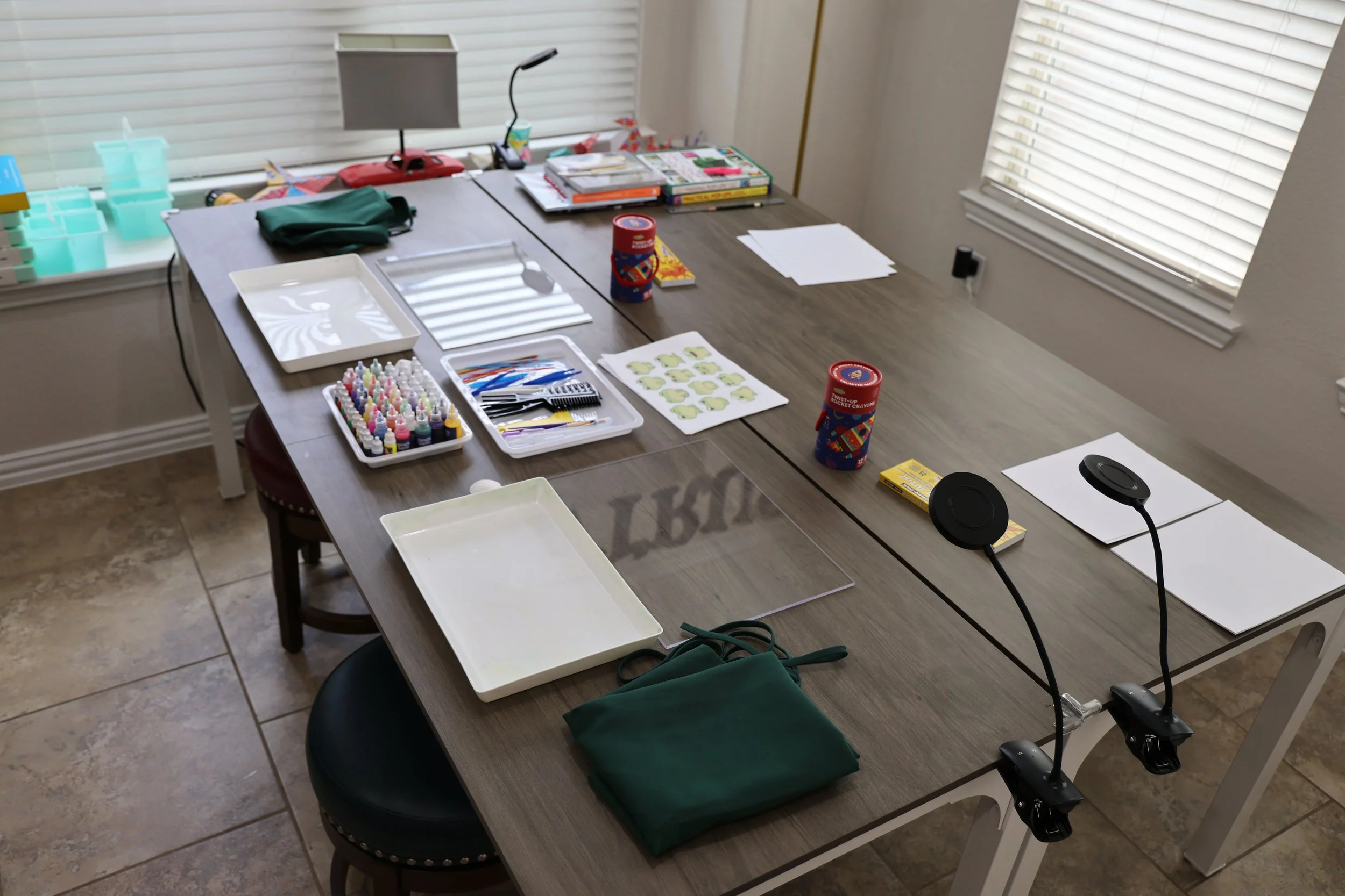 A conference room table set up for a craft activity with supplies like ink bottles, stickers, paper, a lamp, and a pair of microphones.