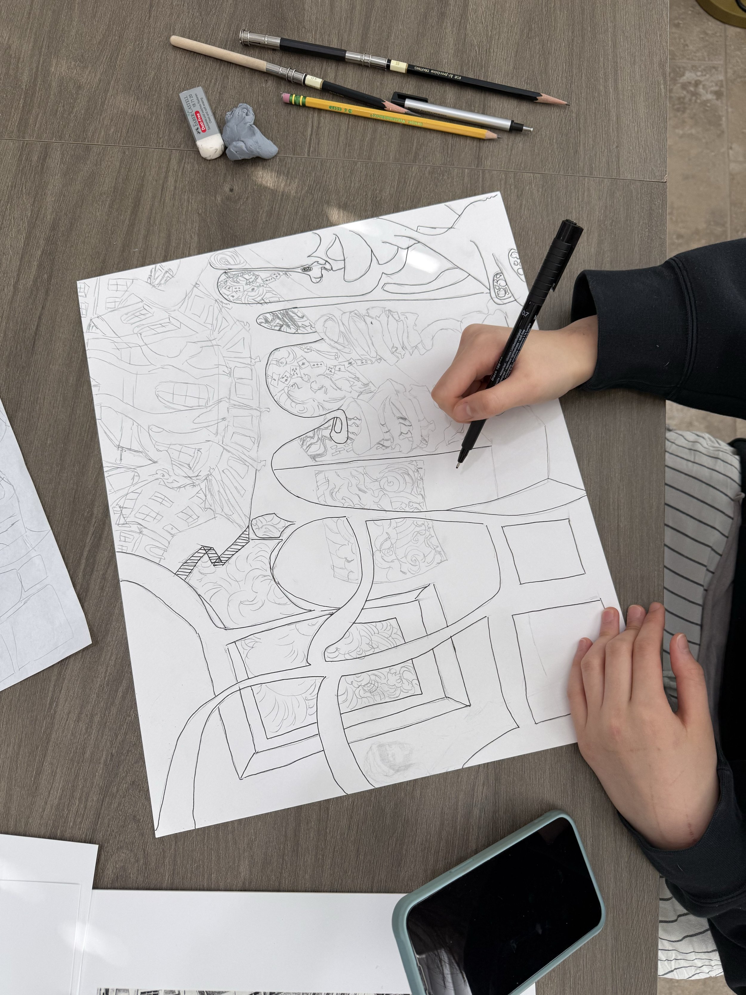 Person drawing a detailed cityscape on a large sheet of paper with various streets, buildings, and architectural elements, using a black marker.