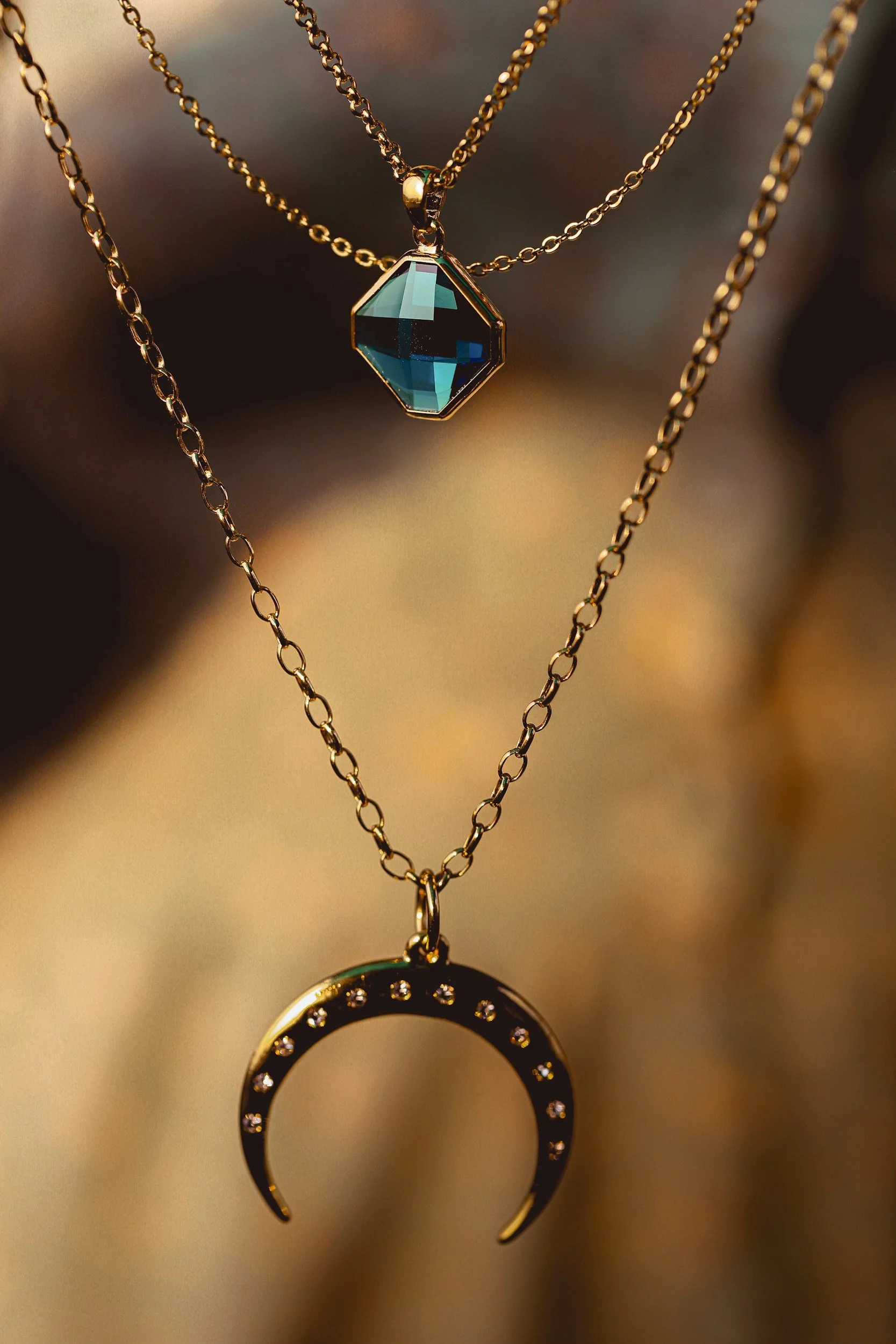 Two layered gold necklaces: one with an octagonal gemstone pendant and the other with a crescent moon pendant with small gemstones.