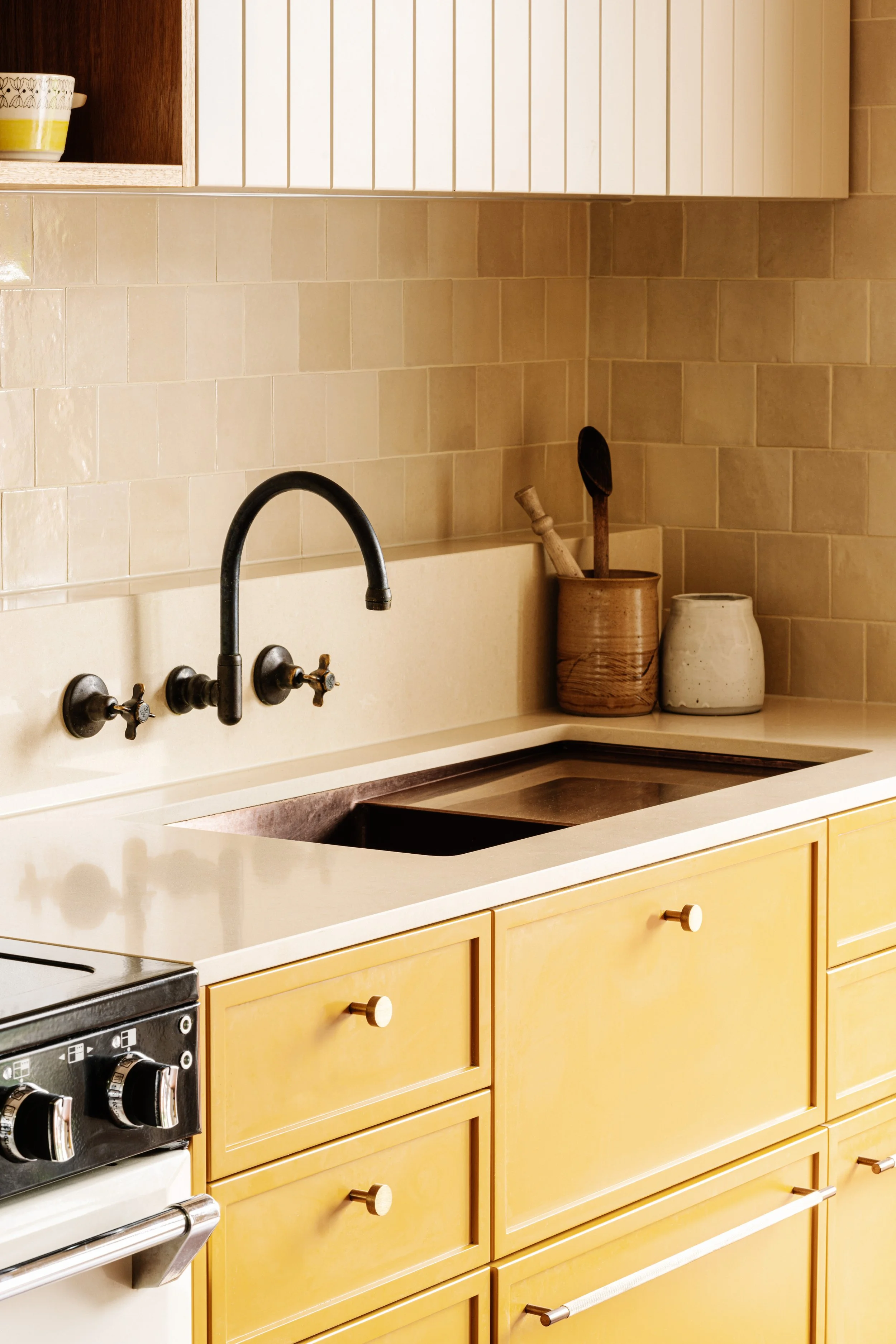 A kitchen with yellow cabinets, beige tiled backsplash, black faucet, a stove, and decorative jars on the countertop.