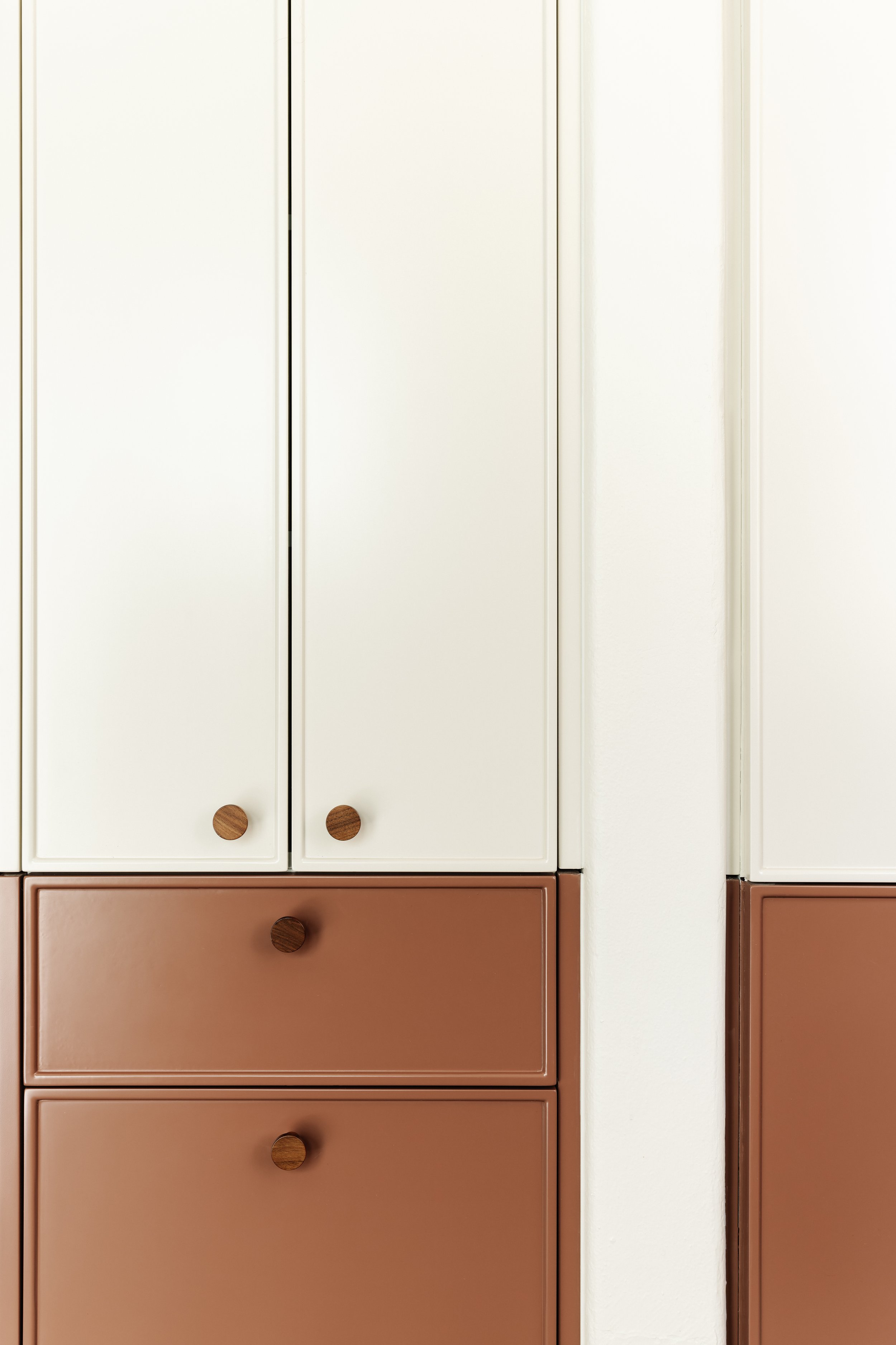 A photo of a storage cabinet with white doors and brown drawers, featuring round wooden knobs.