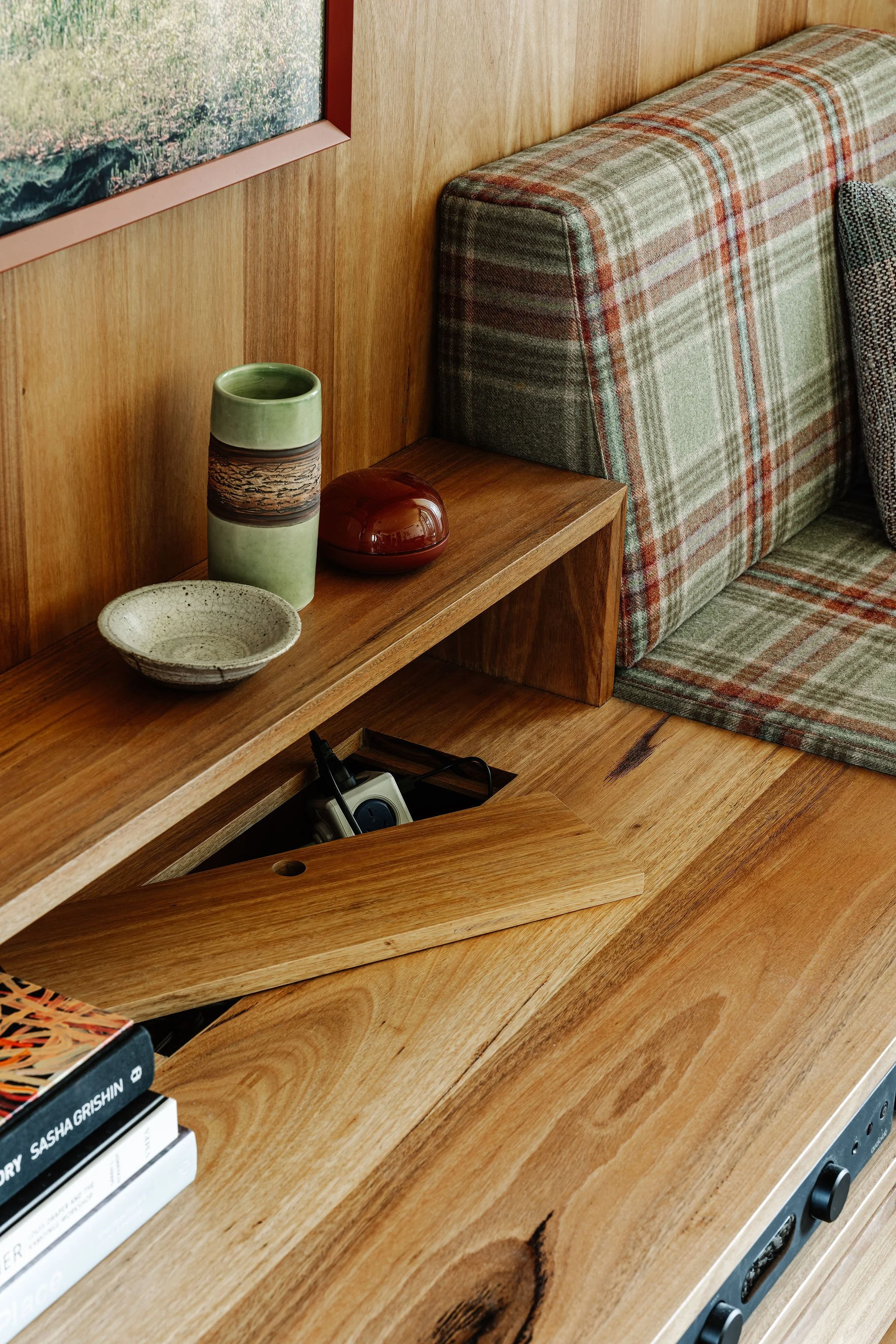 Close-up of a wooden shelf with decorative vases, a bowl, and a portion of a patterned couch against a wooden wall.