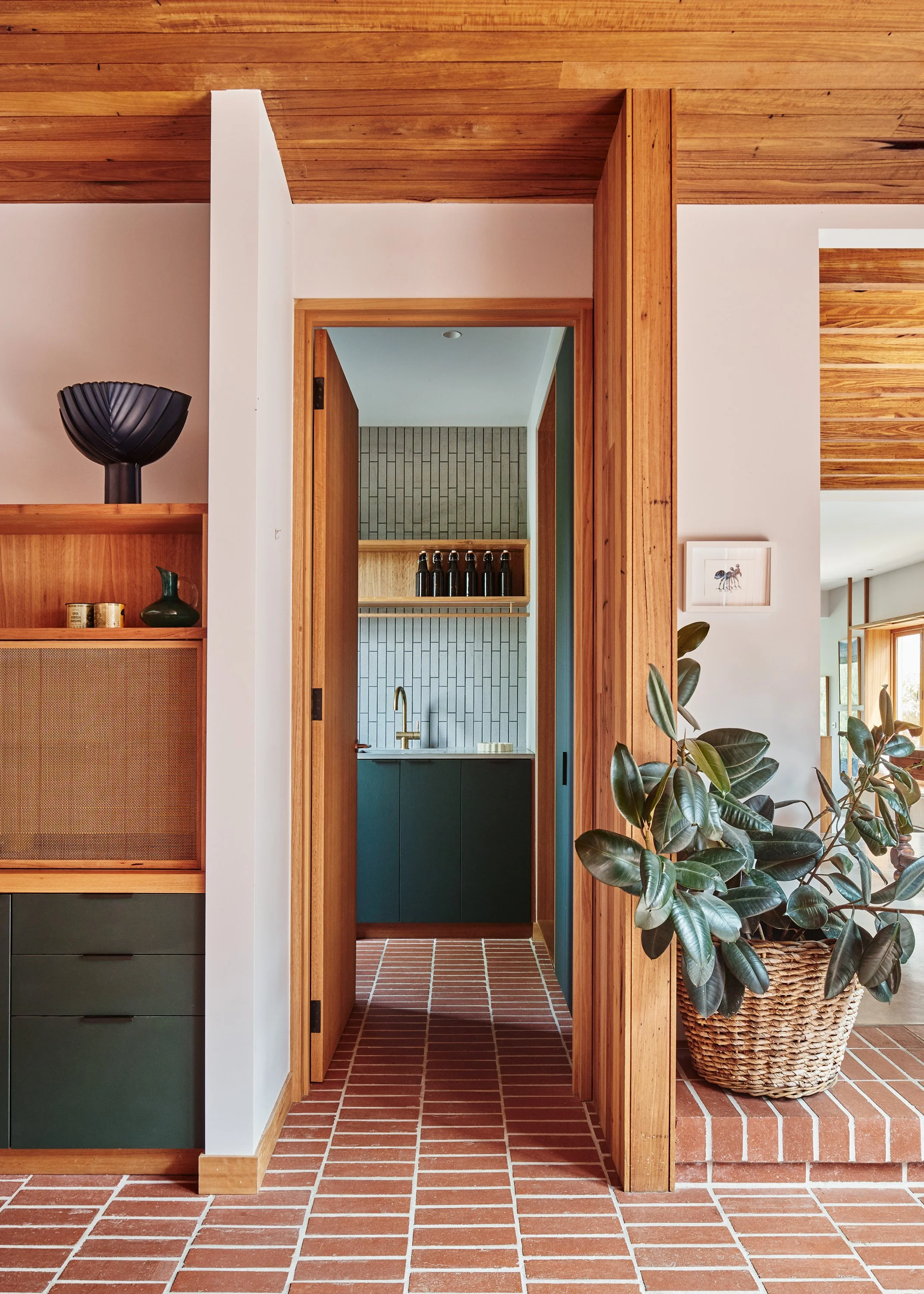 View of wooden and brick interior space with a doorway to a kitchen, green cabinets, and a potted plant.