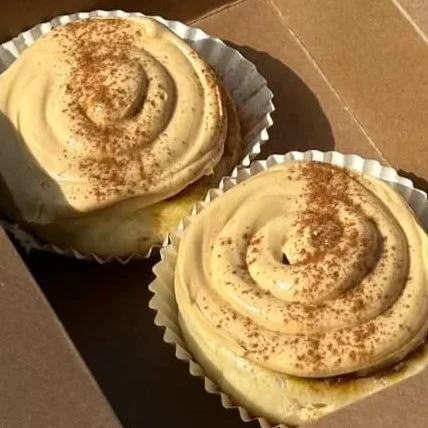 Two cinnamon rolls with cream cheese frosting in a bakery box.