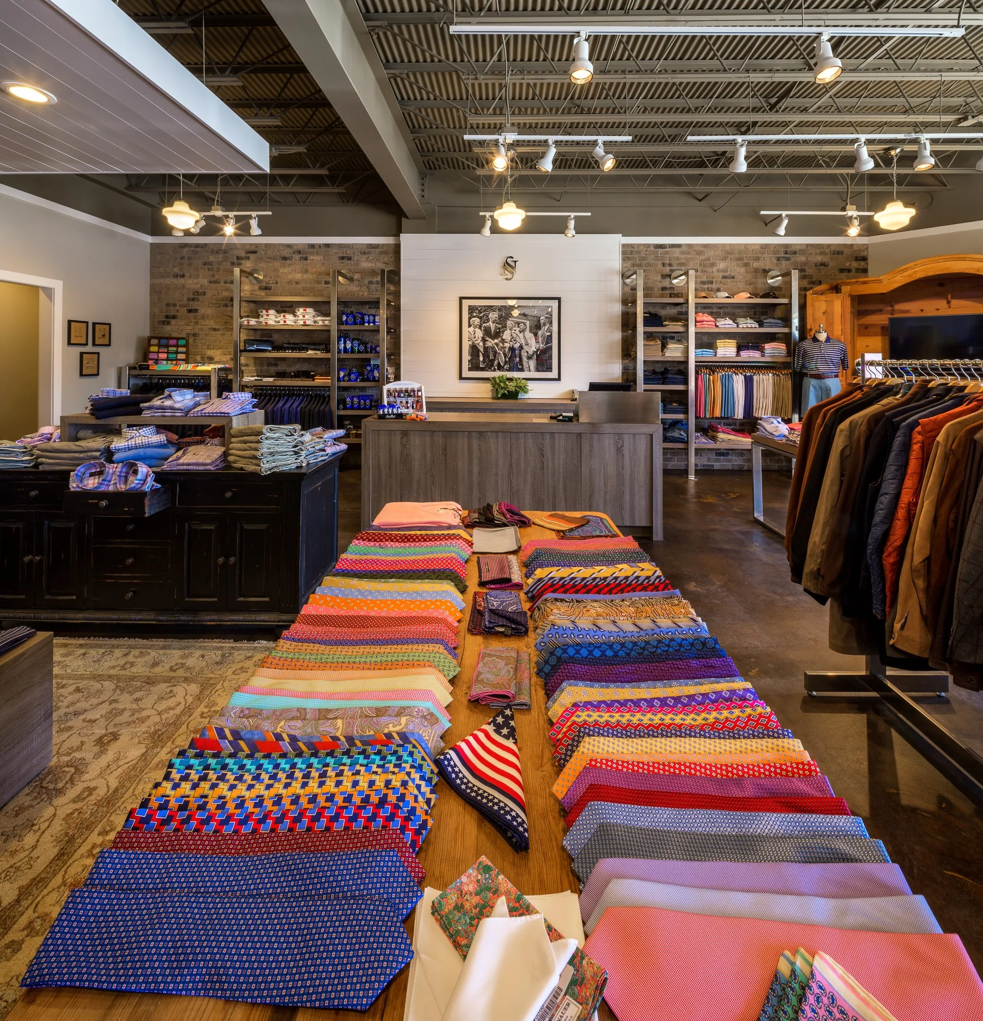 Display of colorful fabrics with assorted patterns on a wooden table inside a clothing store.