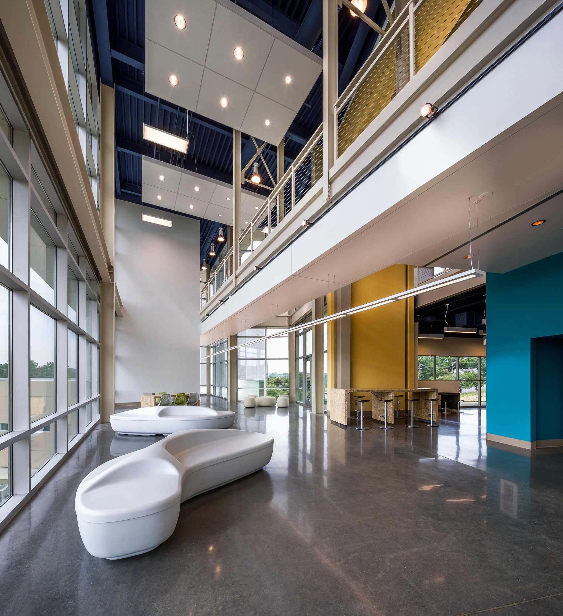 Modern office lobby with large windows, polished concrete floors, white lounge chairs, and a blue accent wall.