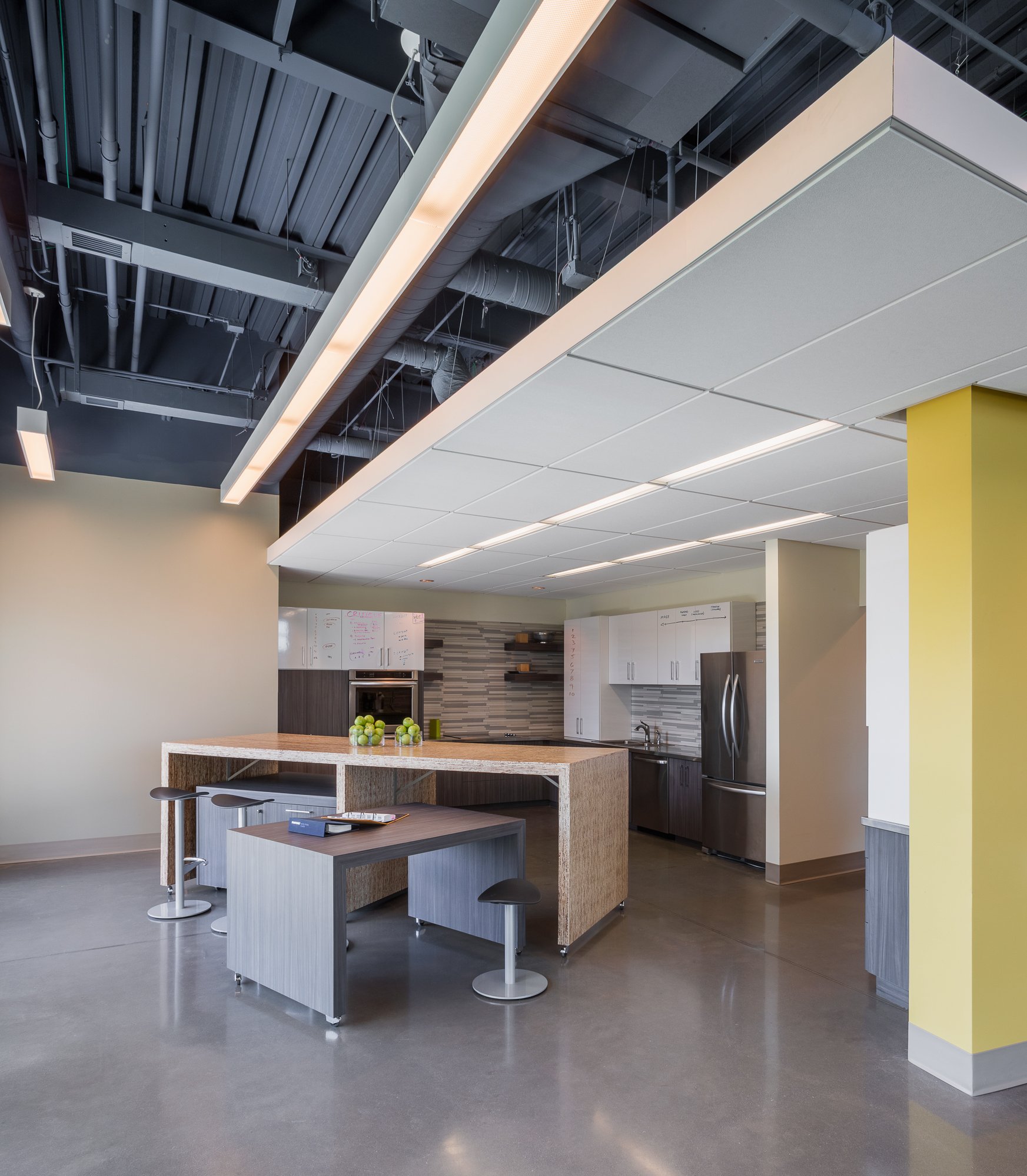 Modern office kitchen with a wooden island, white cabinets, a stainless steel fridge, and a yellow wall.