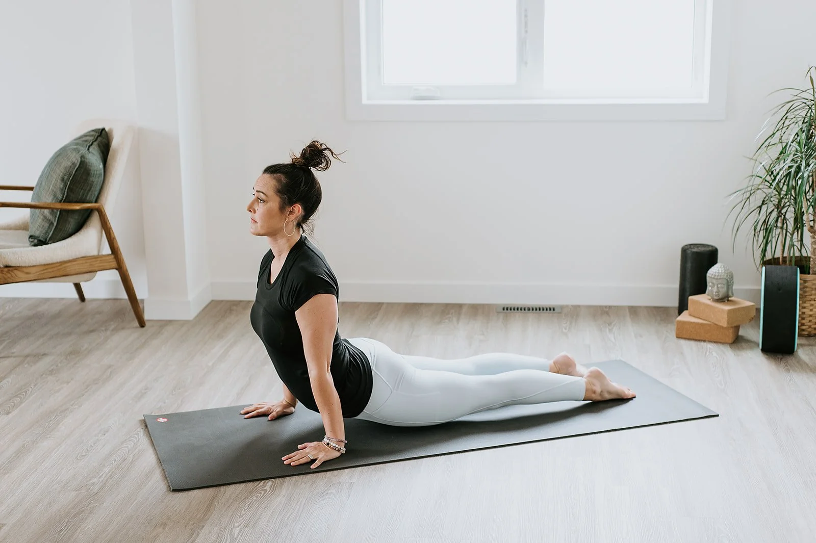 Woman practicing yoga in a bright, minimalist room, performing the cobra pose on a yoga mat.