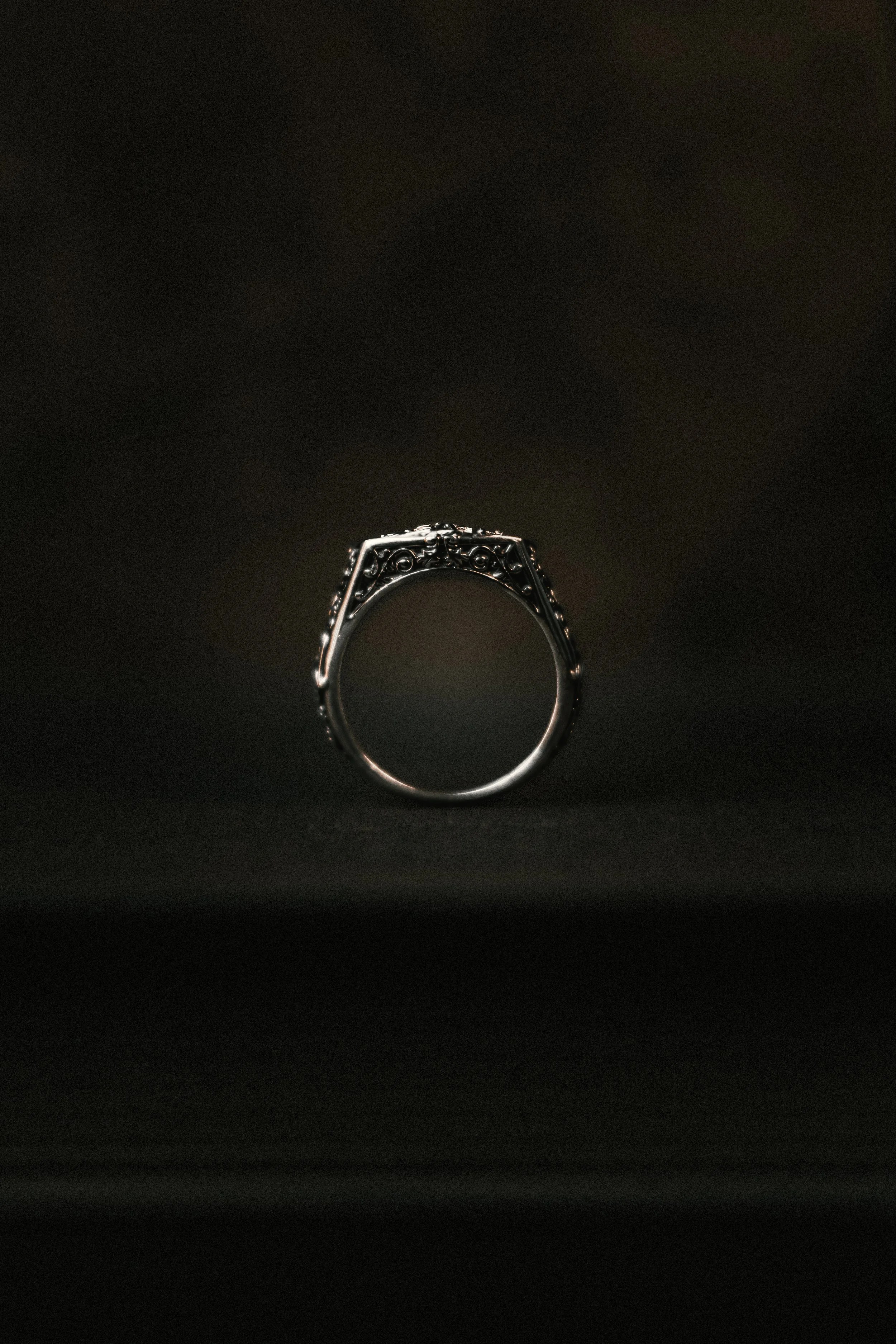 A silver ornate ring displayed against a dark background.