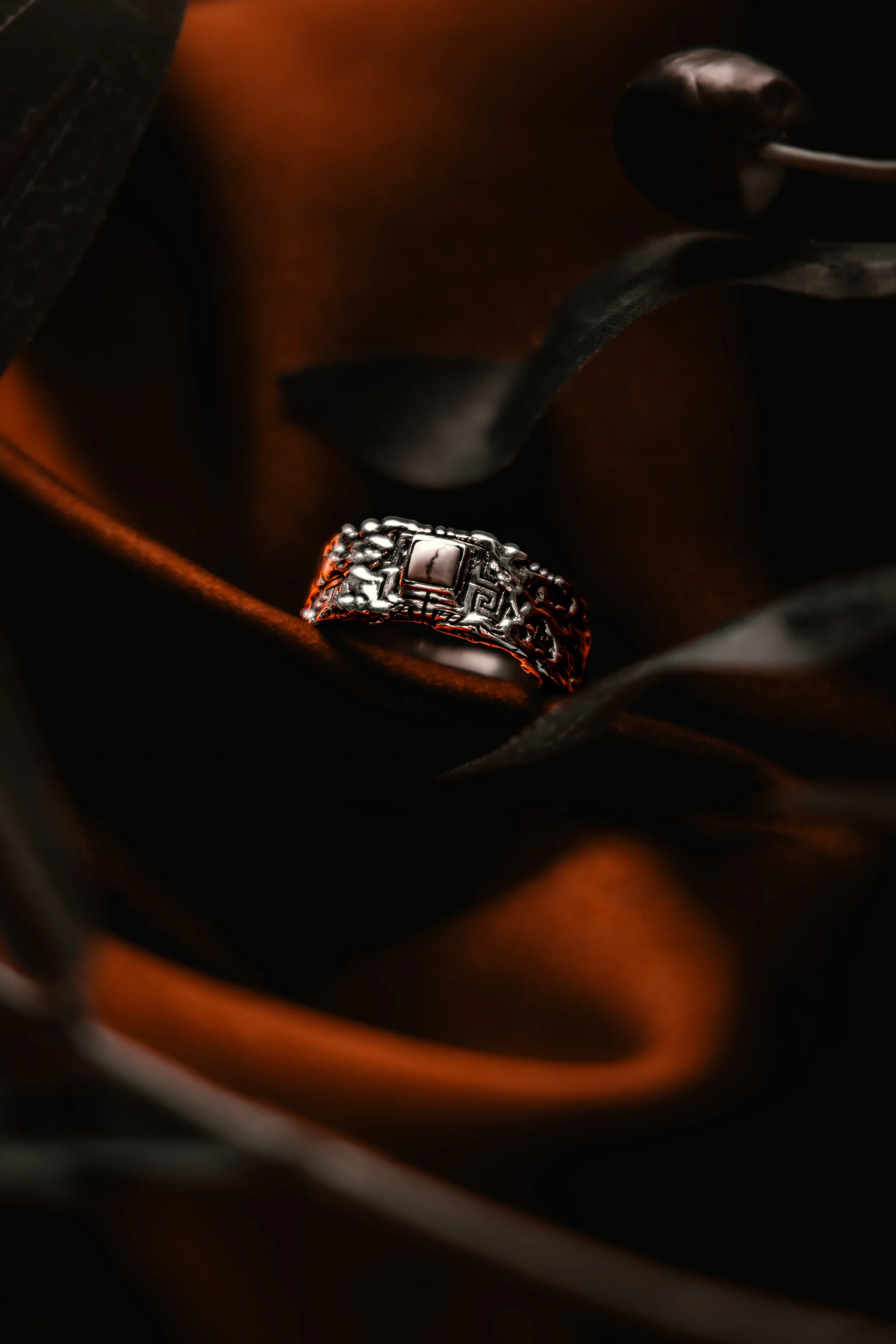 A silver ring with intricate designs resting in a dark, velvet-lined jewelry box.