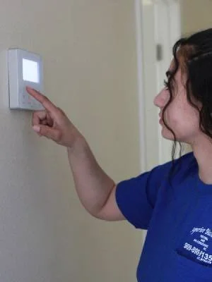 A woman pressing a white button on a wall-mounted device, likely a thermostat or alarm control panel.