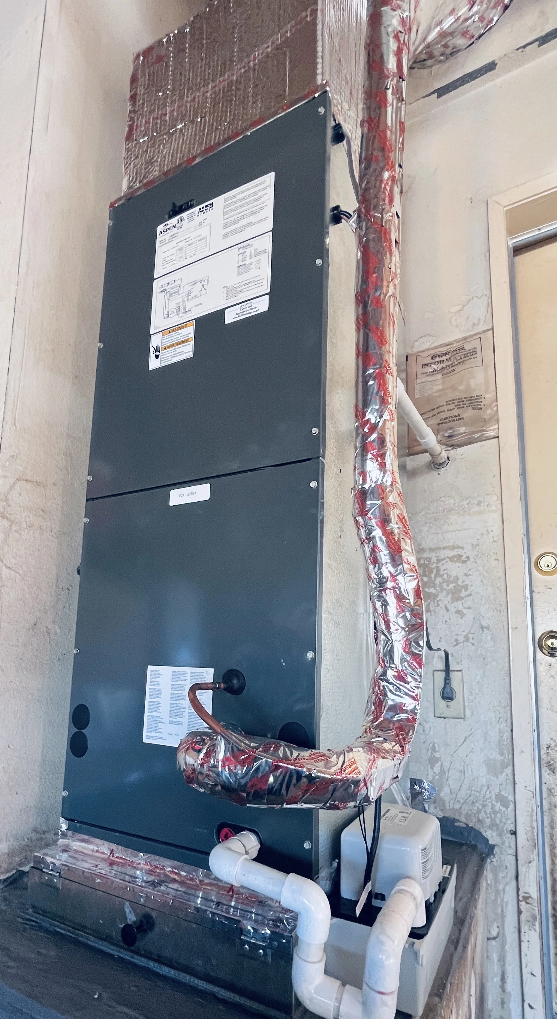 An HVAC unit installed on a wall with insulated pipes, electrical wiring, and a condensate pump nearby.