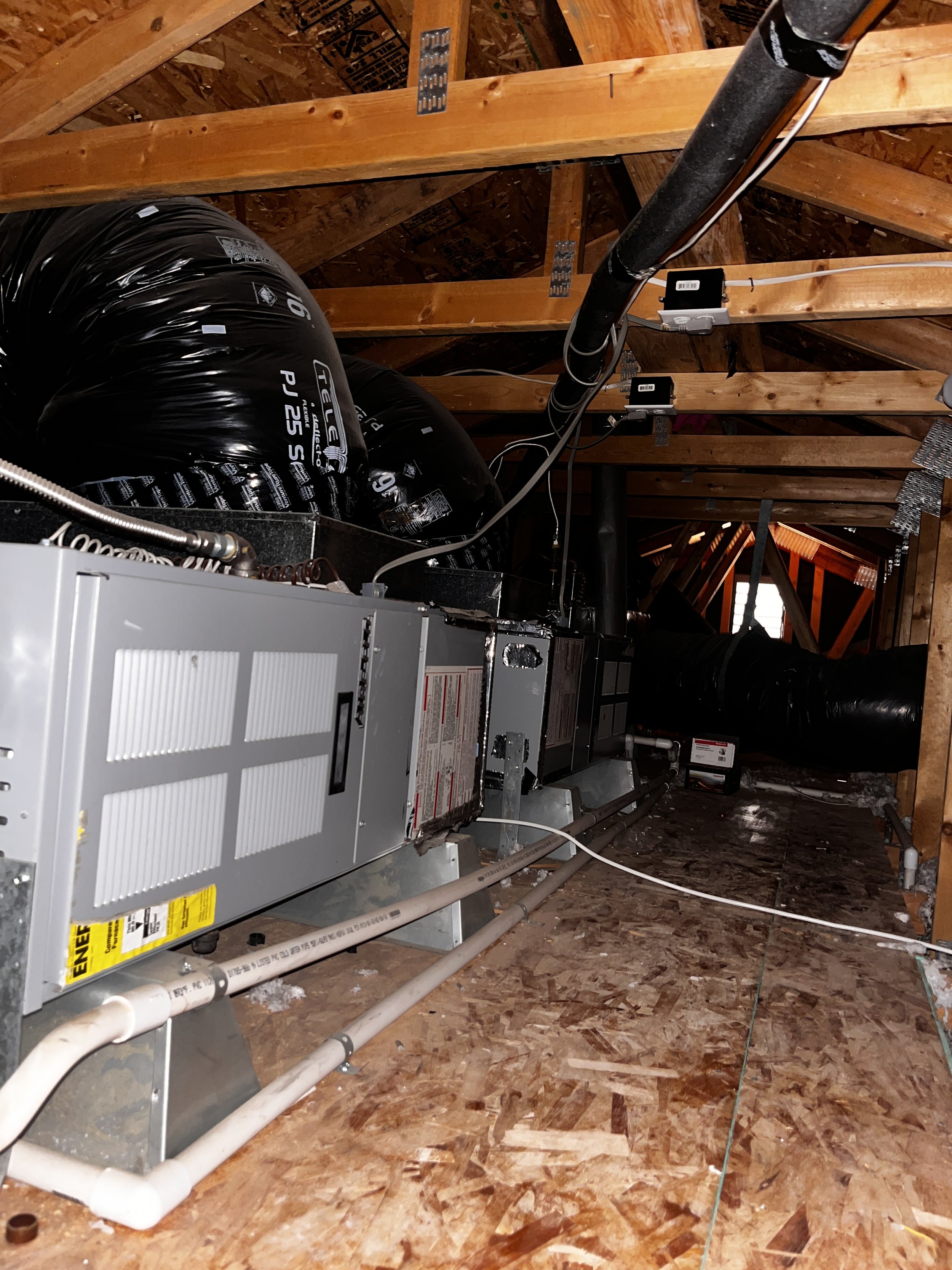 HVAC system installed in an attic space with ductwork, pipes, and electrical wiring visible.