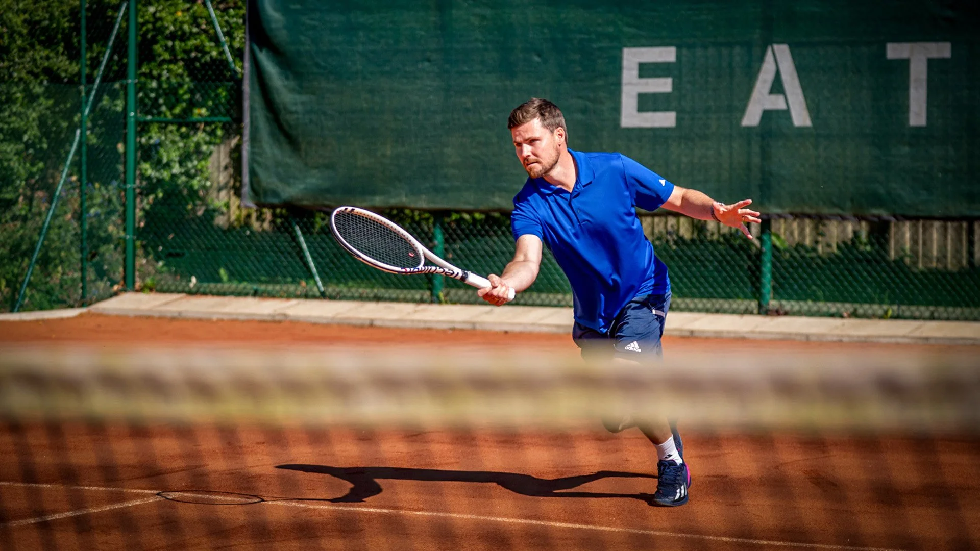 A man playing tennis on a clay court, wearing a blue sports outfit and holding a tennis racket.