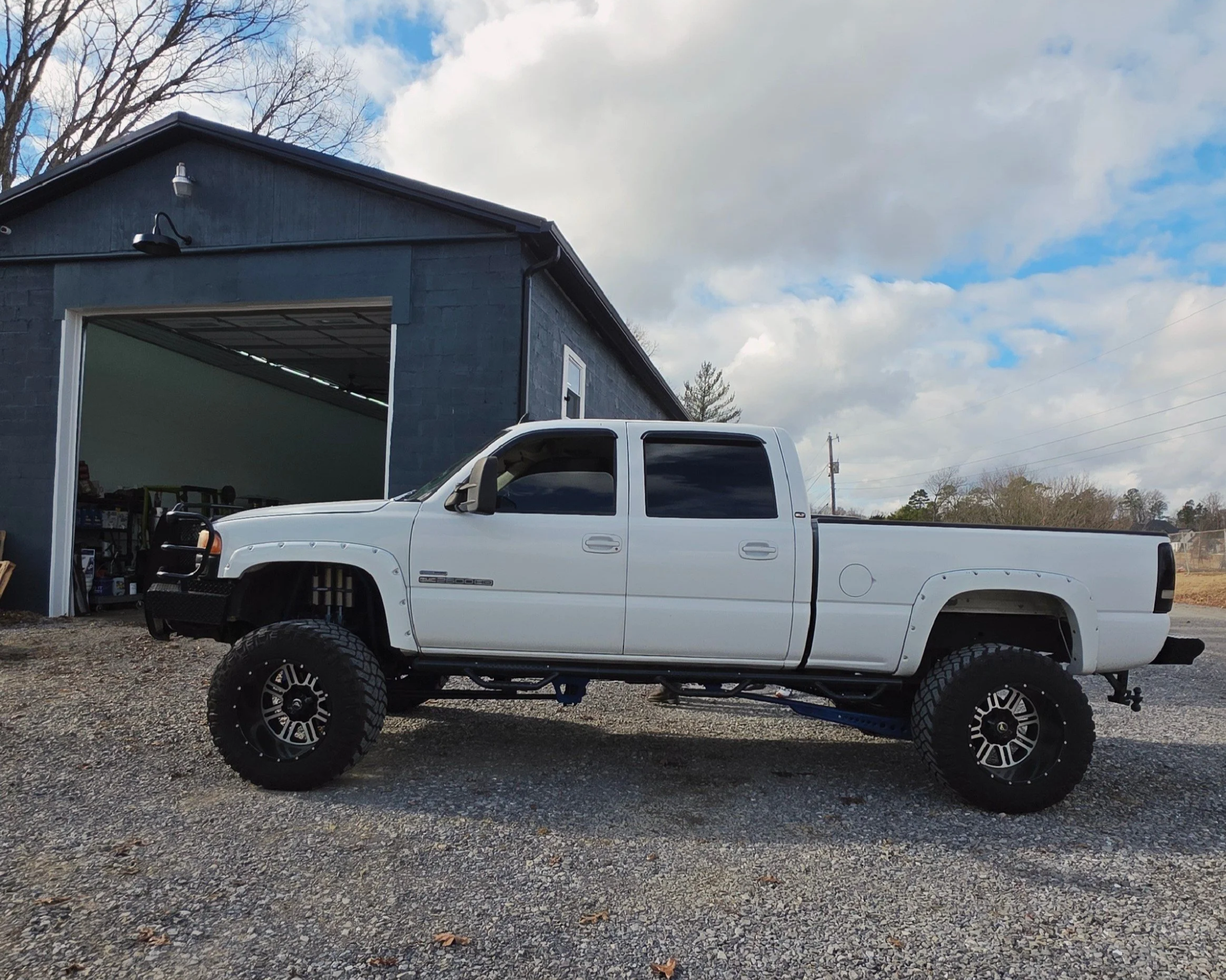 White lifted pickup truck parked outside near a dark gray garage under a cloudy sky.
