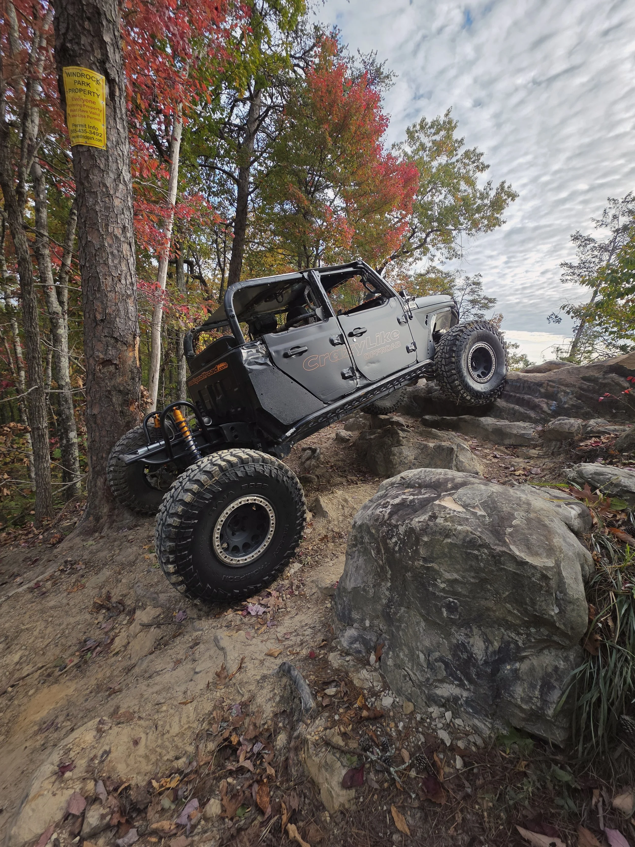 An off-road vehicle, climbing on rocks on a forest trail with colorful autumn trees in the background.