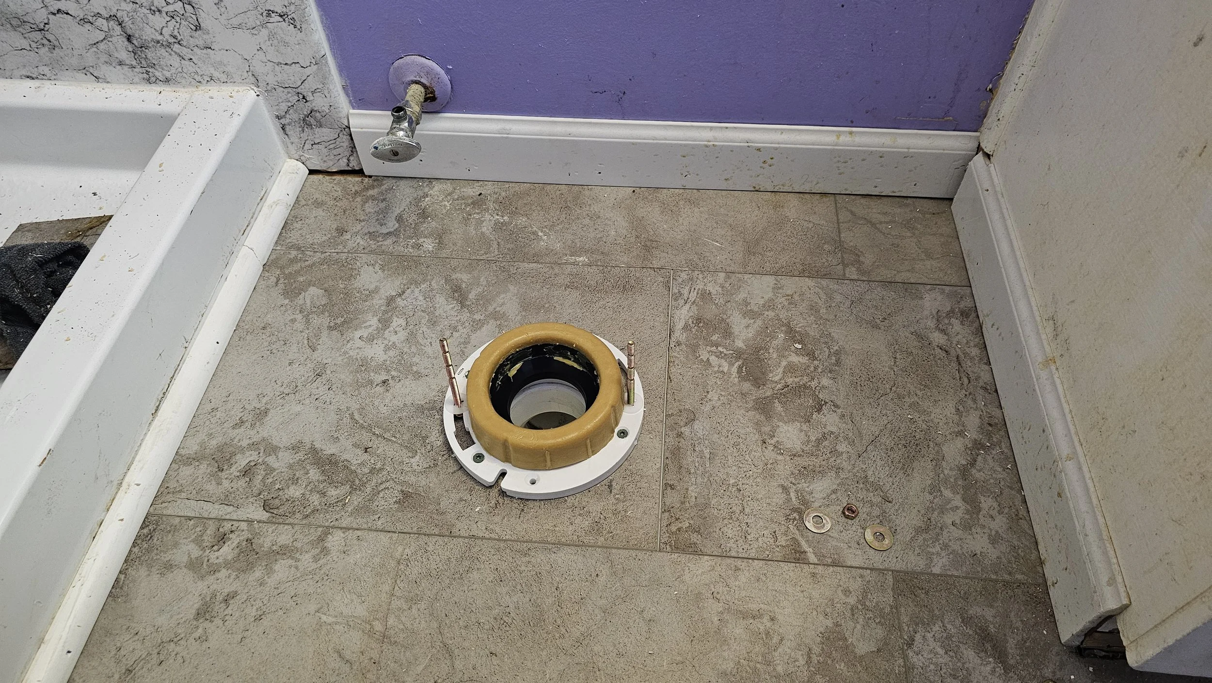 Bathroom floor with plumbing installation ring and a purple wall with damage and dirt