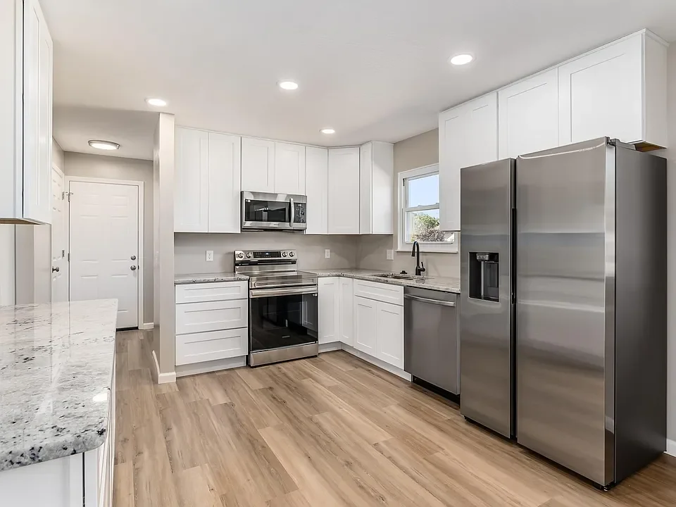 Modern kitchen with white cabinets, stainless steel appliances, a granite countertop, and a light wood floor.