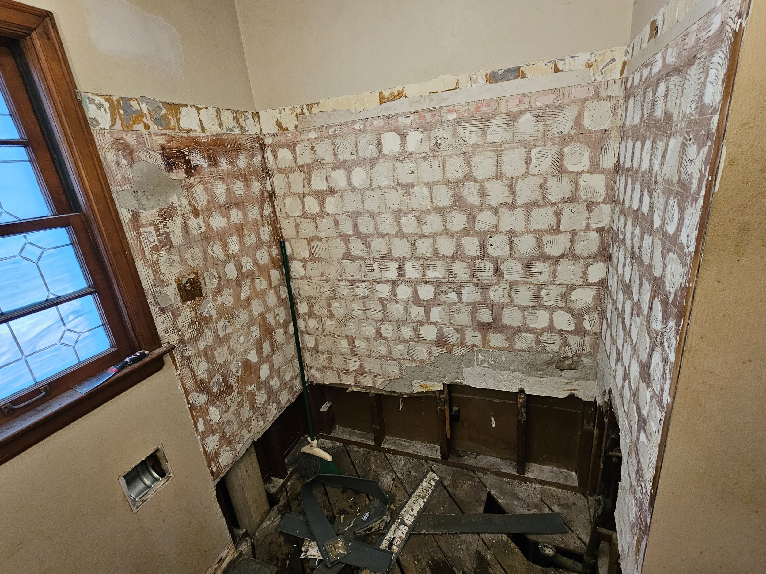 A partially demolished room showing exposed brick walls, a window with a wooden frame, and construction debris on the floor.