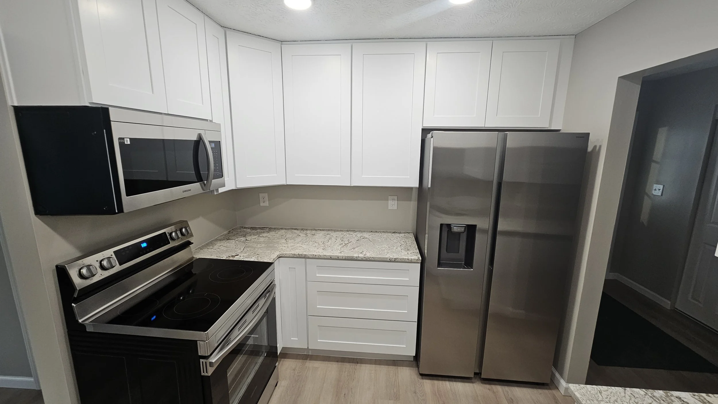 Kitchen with white cabinets, granite countertops, stainless steel refrigerator, microwave, and oven.
