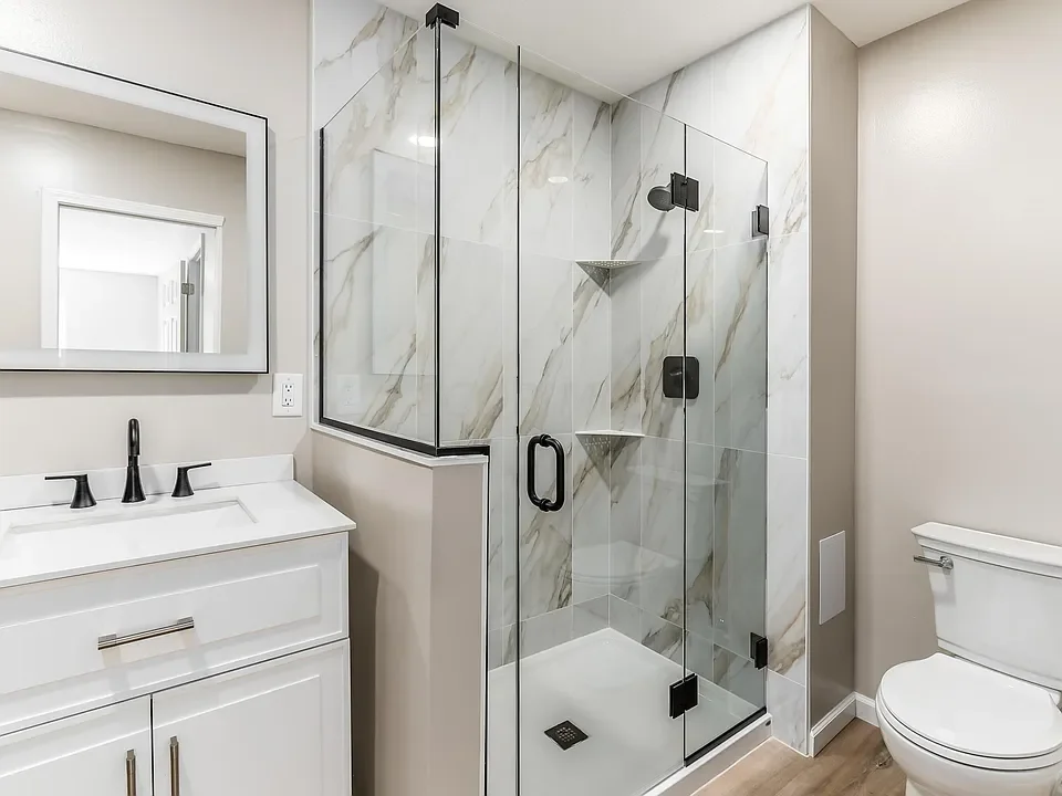 A modern bathroom with a glass-enclosed shower, white vanity with black fixtures, large mirror, and a toilet.
