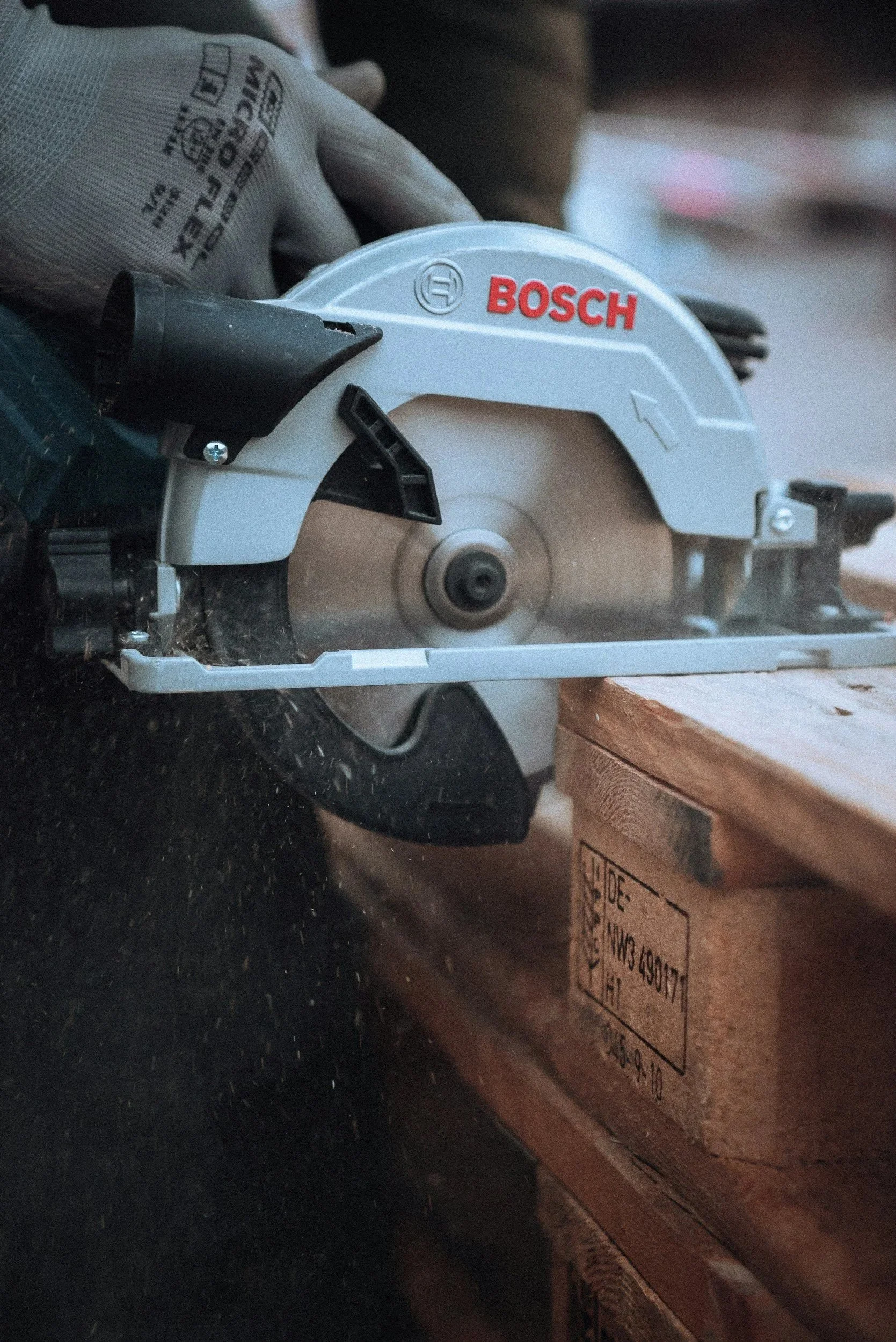 A person wearing gloves using a Bosch circular saw to cut a piece of wood on a workbench.