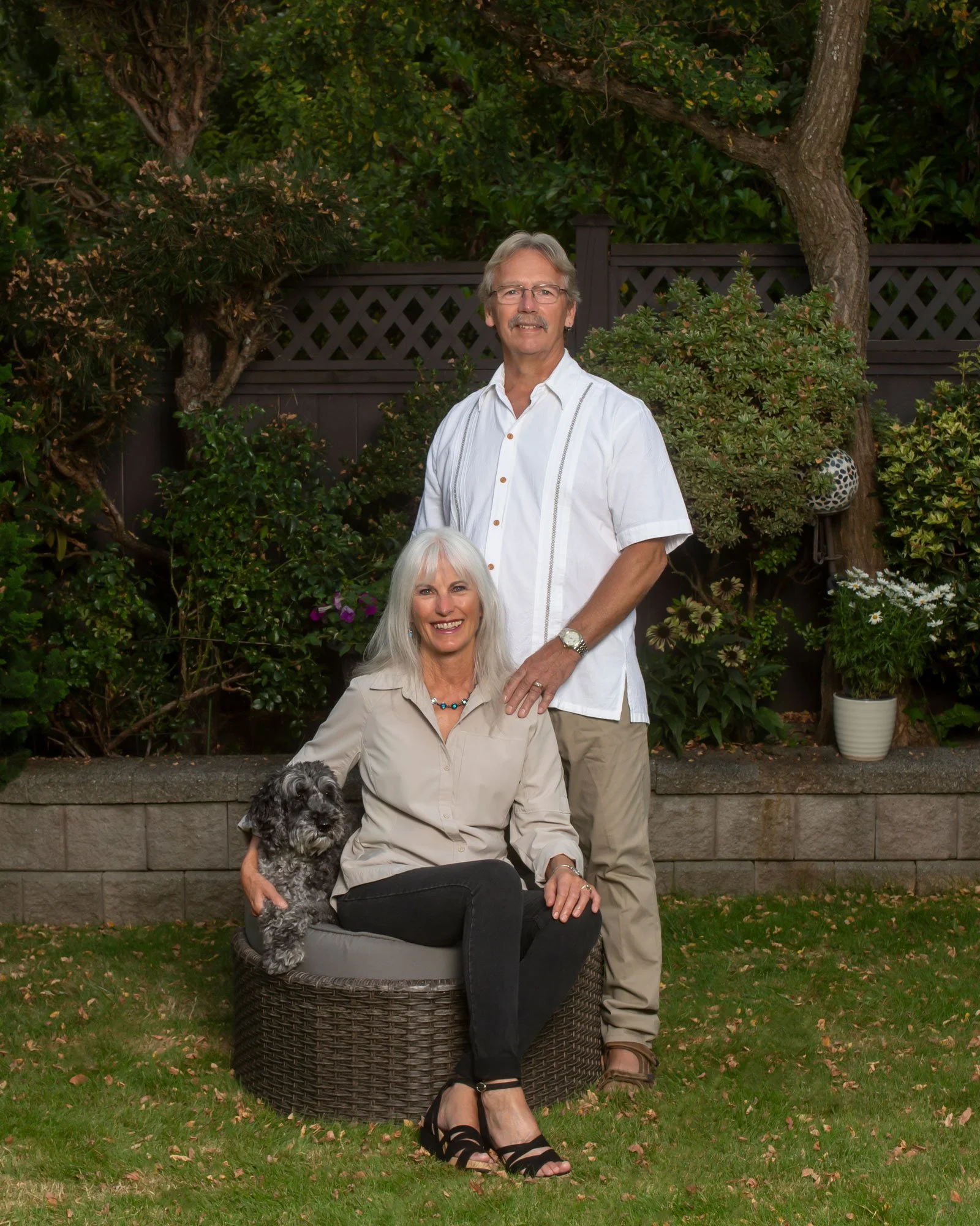 Outdoor portrait of a couple with their dog in a garden with natural greenery.