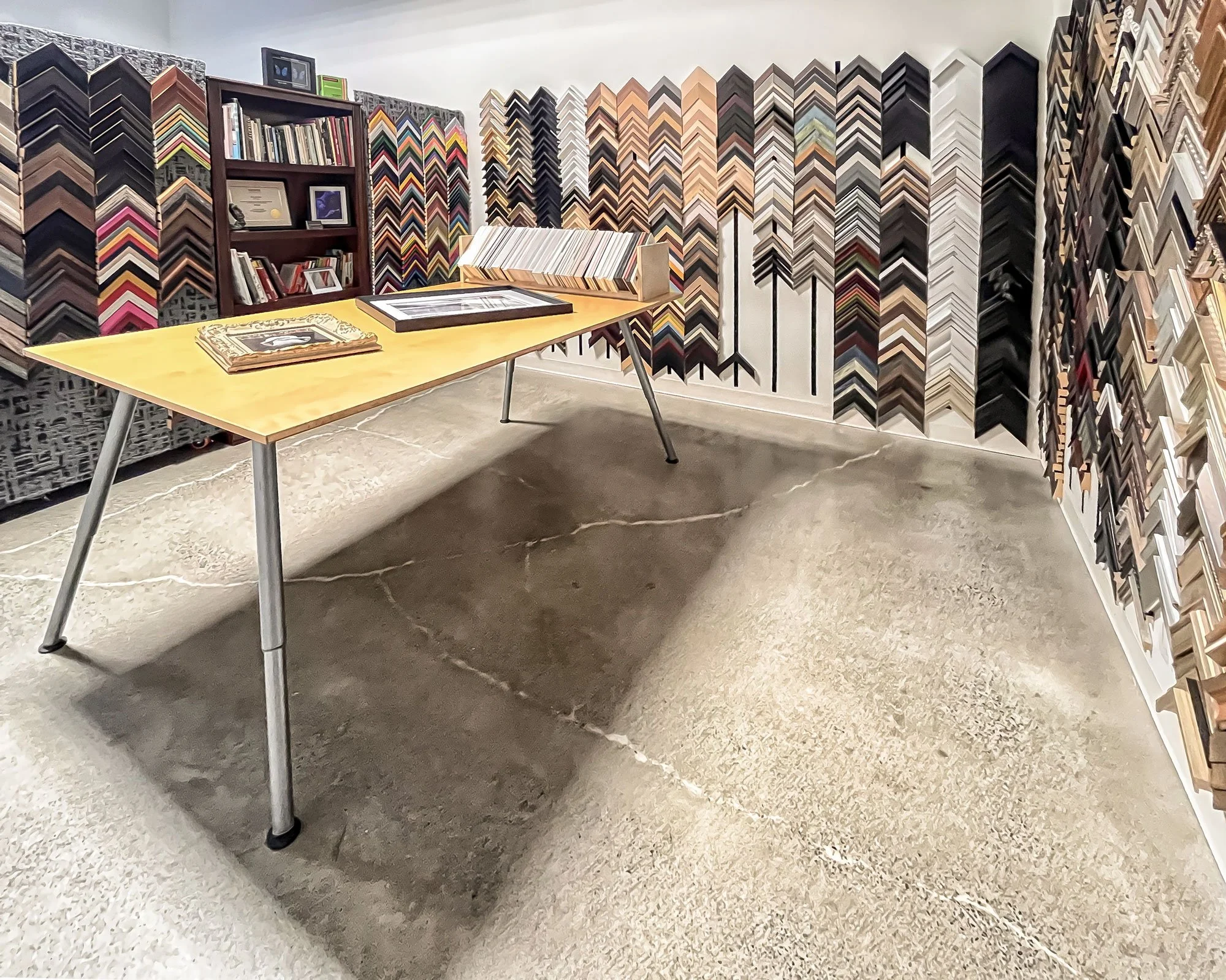 Custom picture framing studio in Mount Pleasant, Vancouver, featuring a curated wall of frame samples and in-studio design table at Legere Fine Art Services.