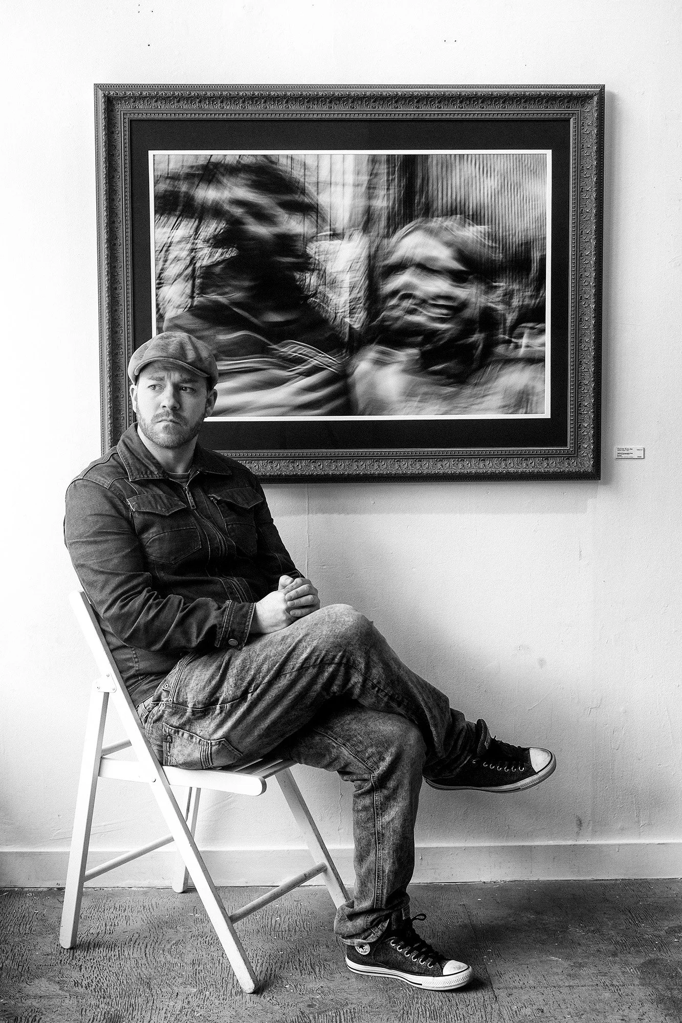 Portrait of Andrew Legere, founder of Legere Fine Art Services, seated in front of a framed photograph in a Vancouver gallery.