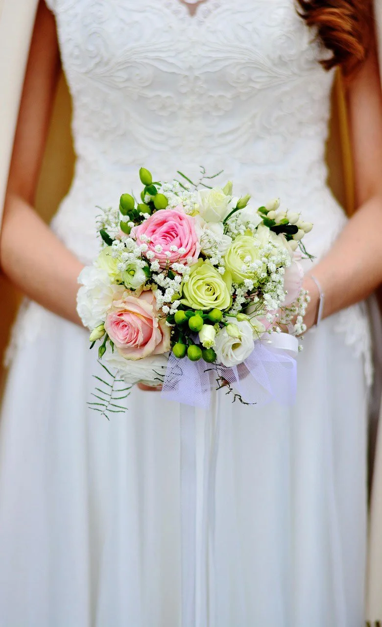 A bride wearing a white wedding dress holding a bouquet of pink, white, and green flowers, including roses and baby's breath.