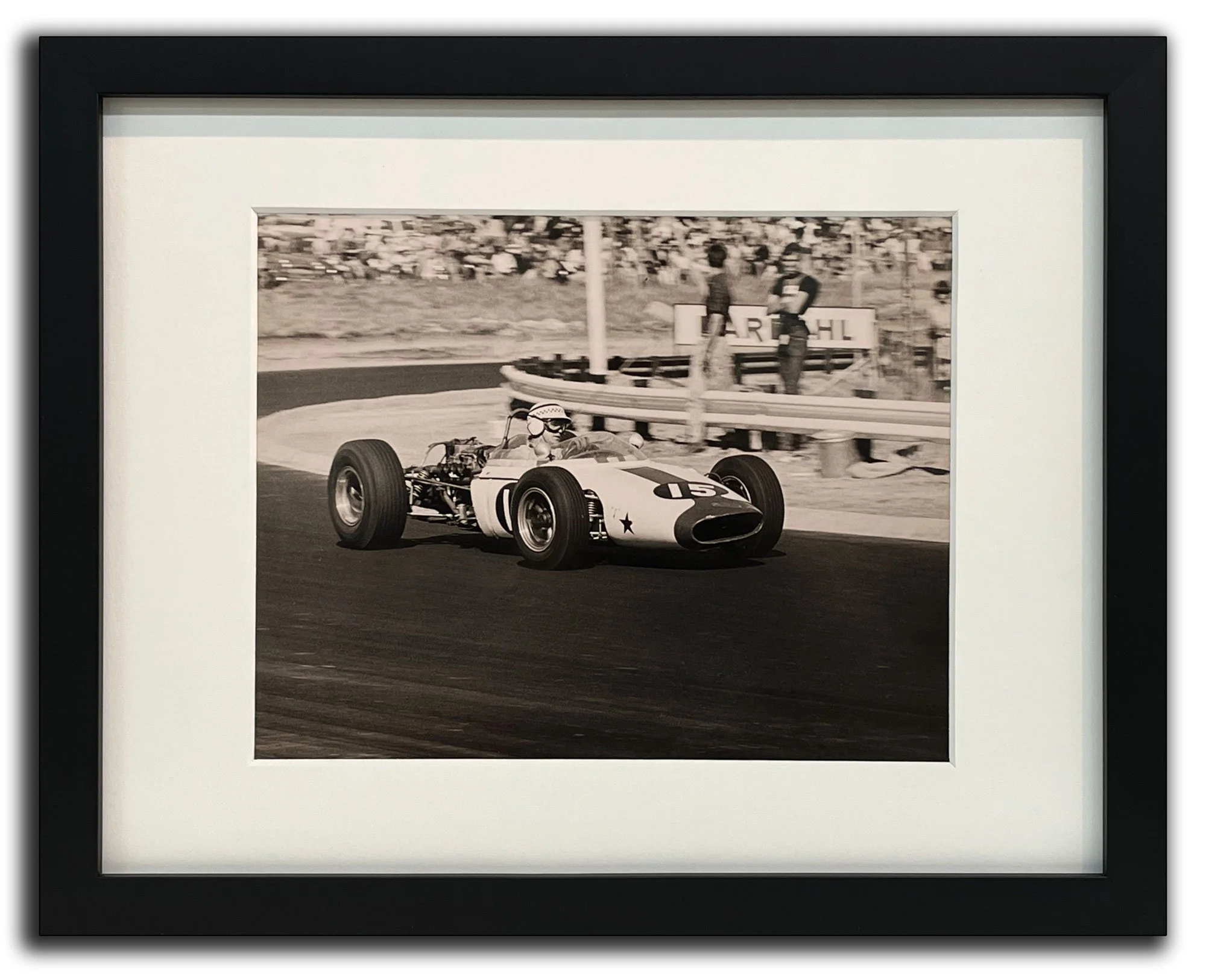 Black and white photograph of a vintage Formula 1 race car during a race, with drivers and spectators in the background.