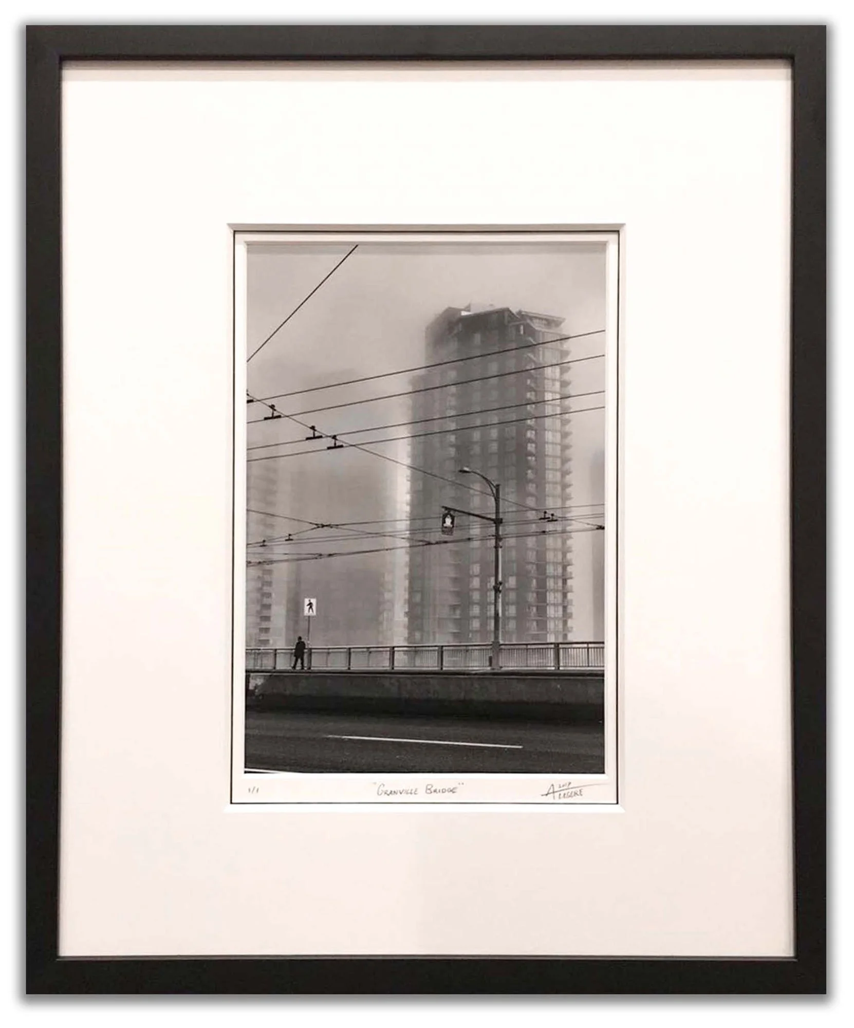 Framed artwork depicting a foggy cityscape with a partially constructed high-rise building, power lines, and a pedestrian walking on a bridge, titled 'Granville Bridge'.