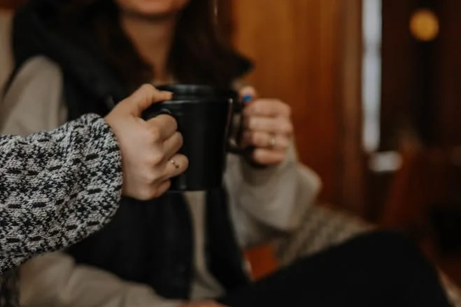 Two women exchanging a black mug in a warmly lit indoor setting.