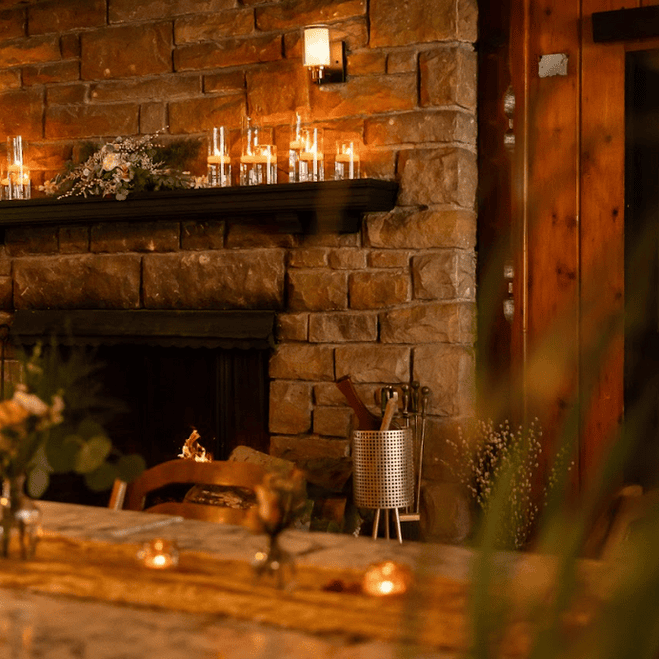 Cozy rustic living room with a brick fireplace, wooden wall, candles on the mantle, and soft lighting.