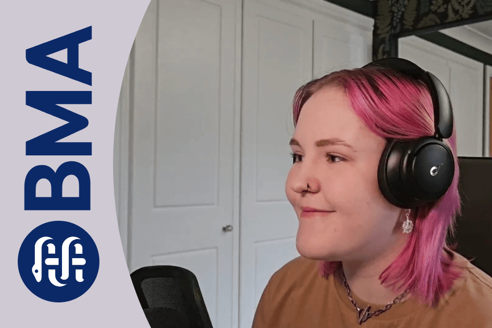 Side-on photo of Lozza sat at their desk smiling while doing an online panel for the BMA. They have light pink shoulder-length hair, and are wearing a beige tshirt and black headphones. Overlaid on this is a lilac swoosh with the BMA logo on it.