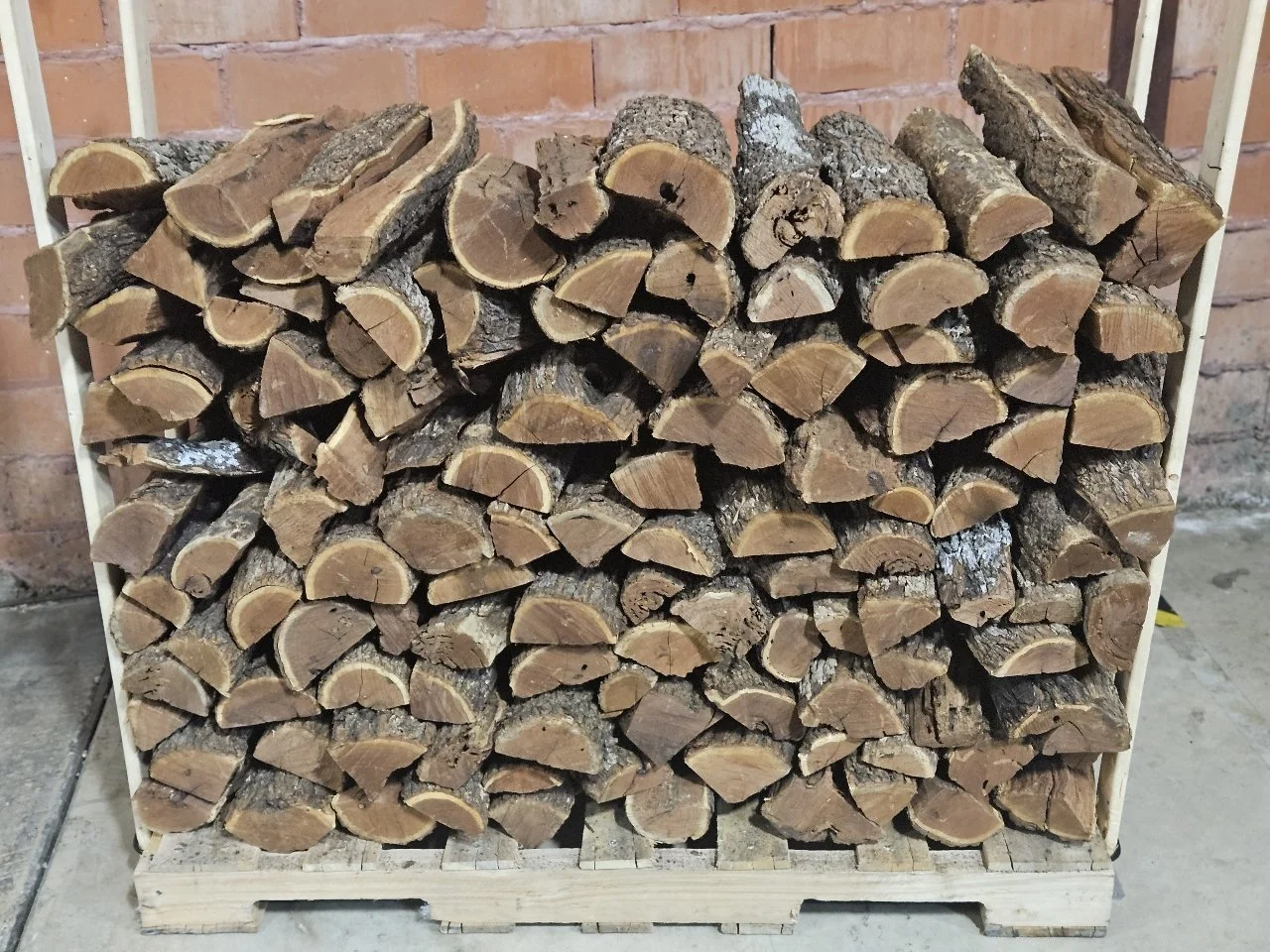 Stack of firewood logs on a wooden pallet against a brick wall.