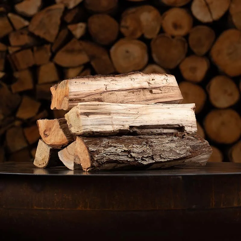 Stack of chopped firewood logs on a dark surface, with more logs in the background.