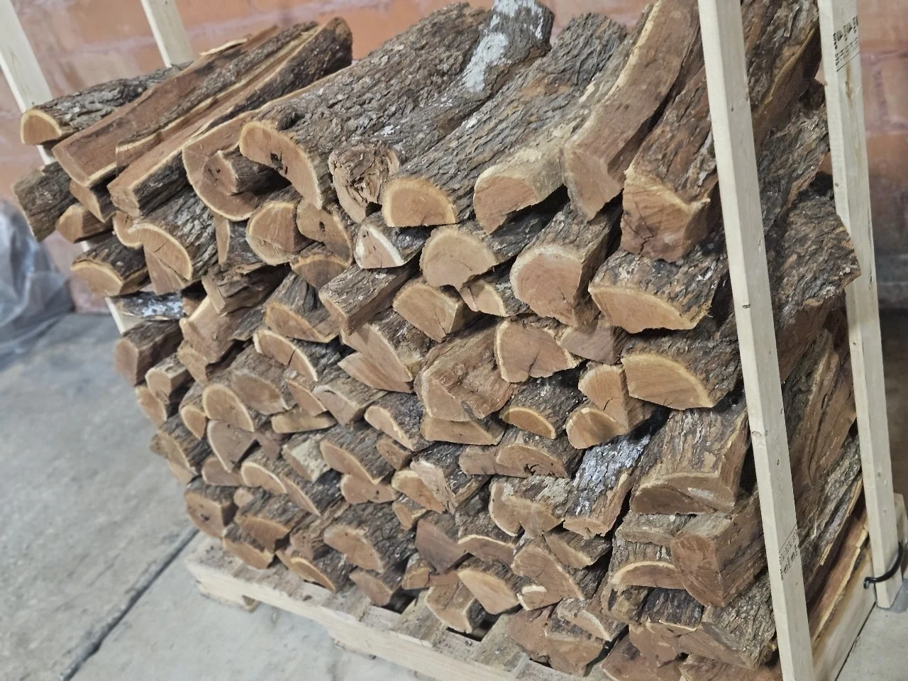 A stack of chopped firewood logs arranged on a wooden pallet in a storage area.