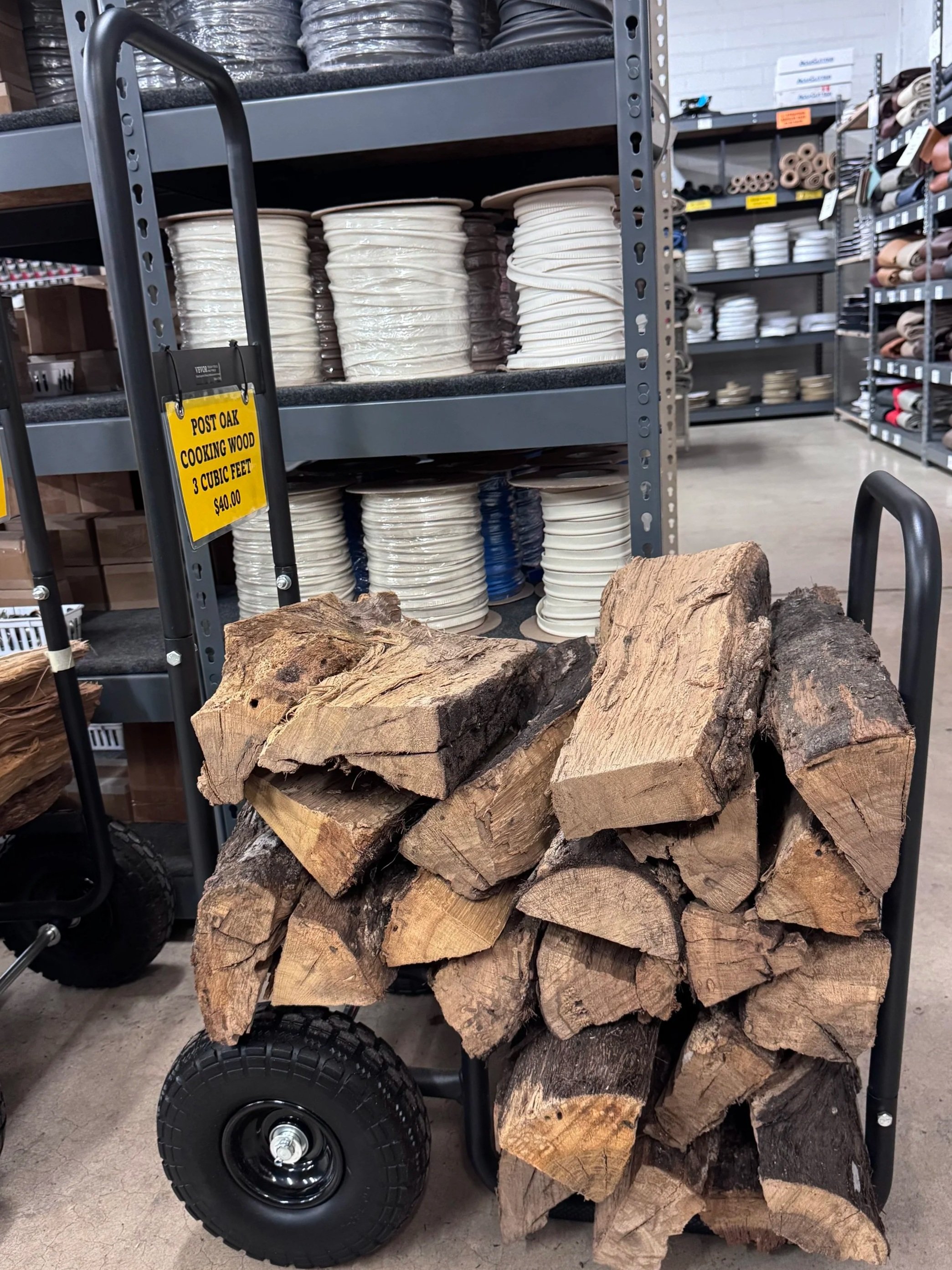 A cart loaded with stacked firewood in front of store shelves with ceramic plates and other supplies.