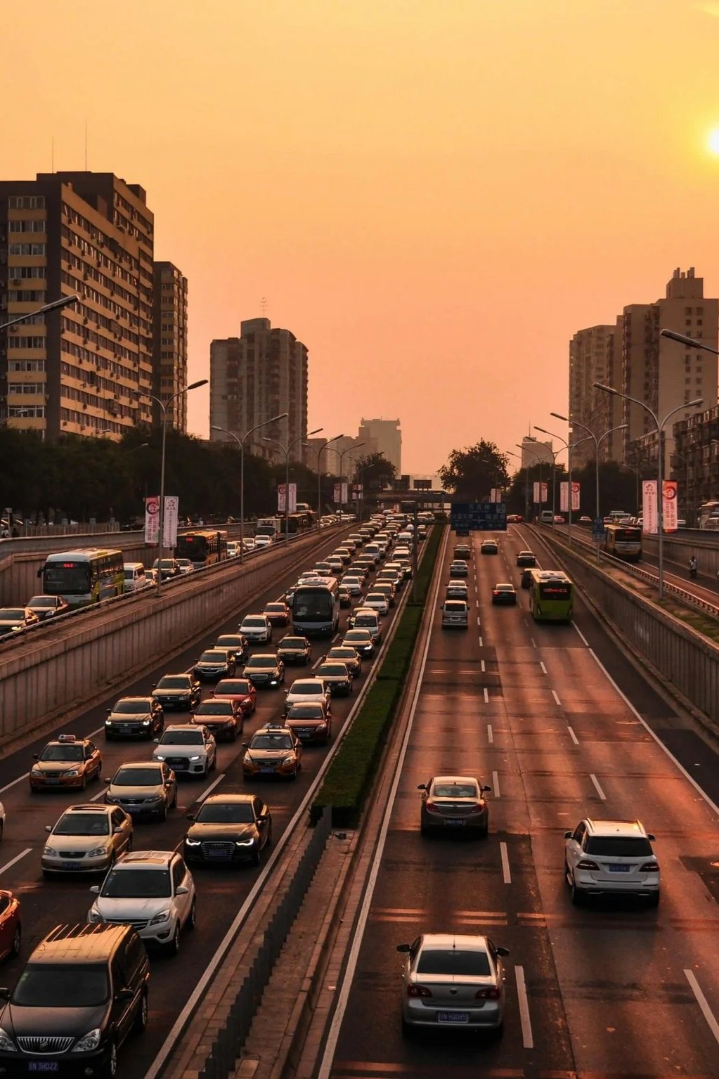 A city street during sunset with high-rise buildings, a mix of congested traffic on the left and fewer cars on the right, and a warm orange sky.