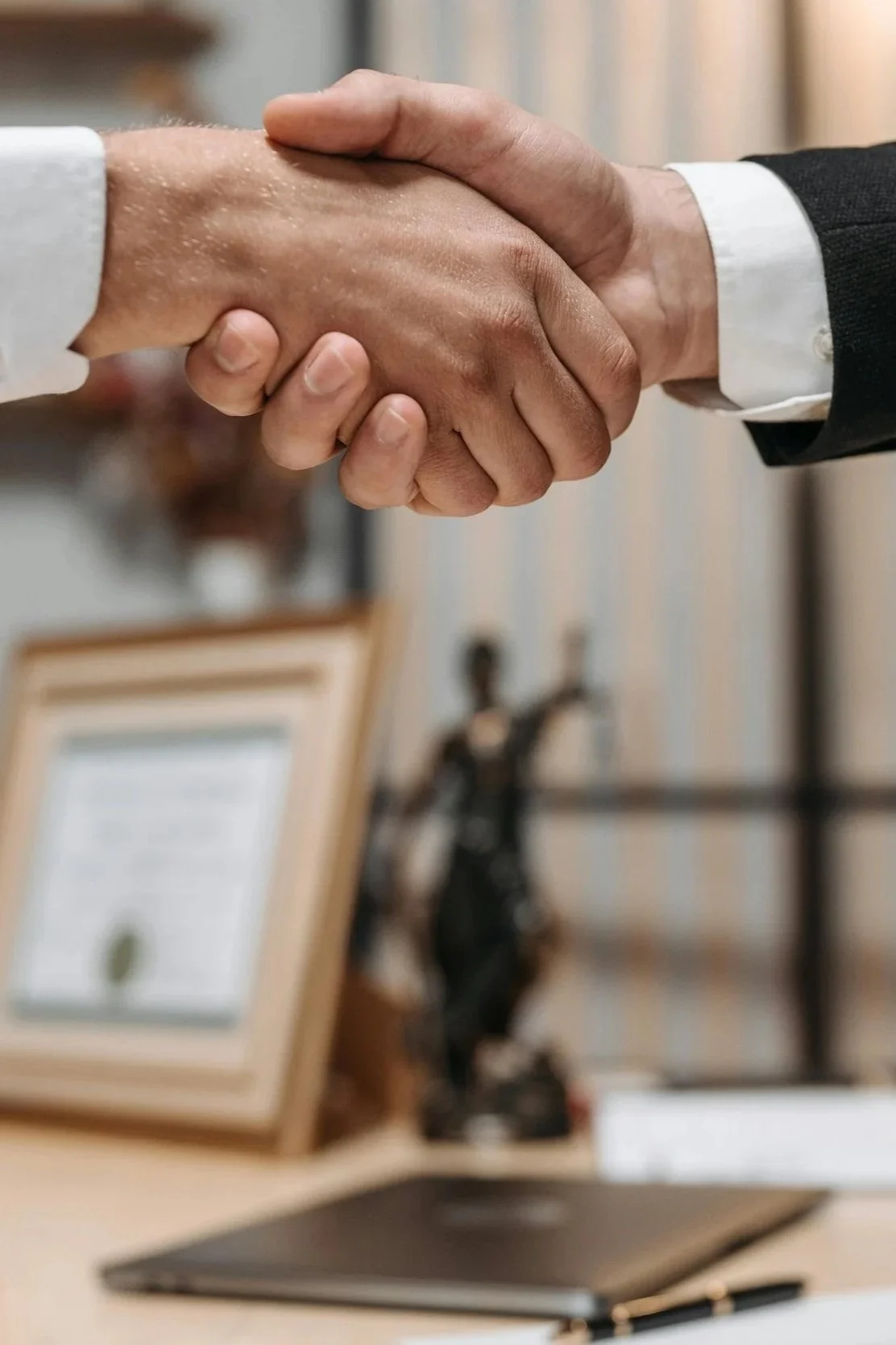 Close-up of two people shaking hands, one in a light-colored shirt and the other in a dark suit, in an office setting.