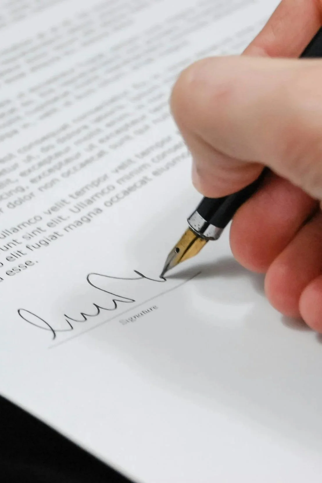 A person signing a document with a black fountain pen on white paper.