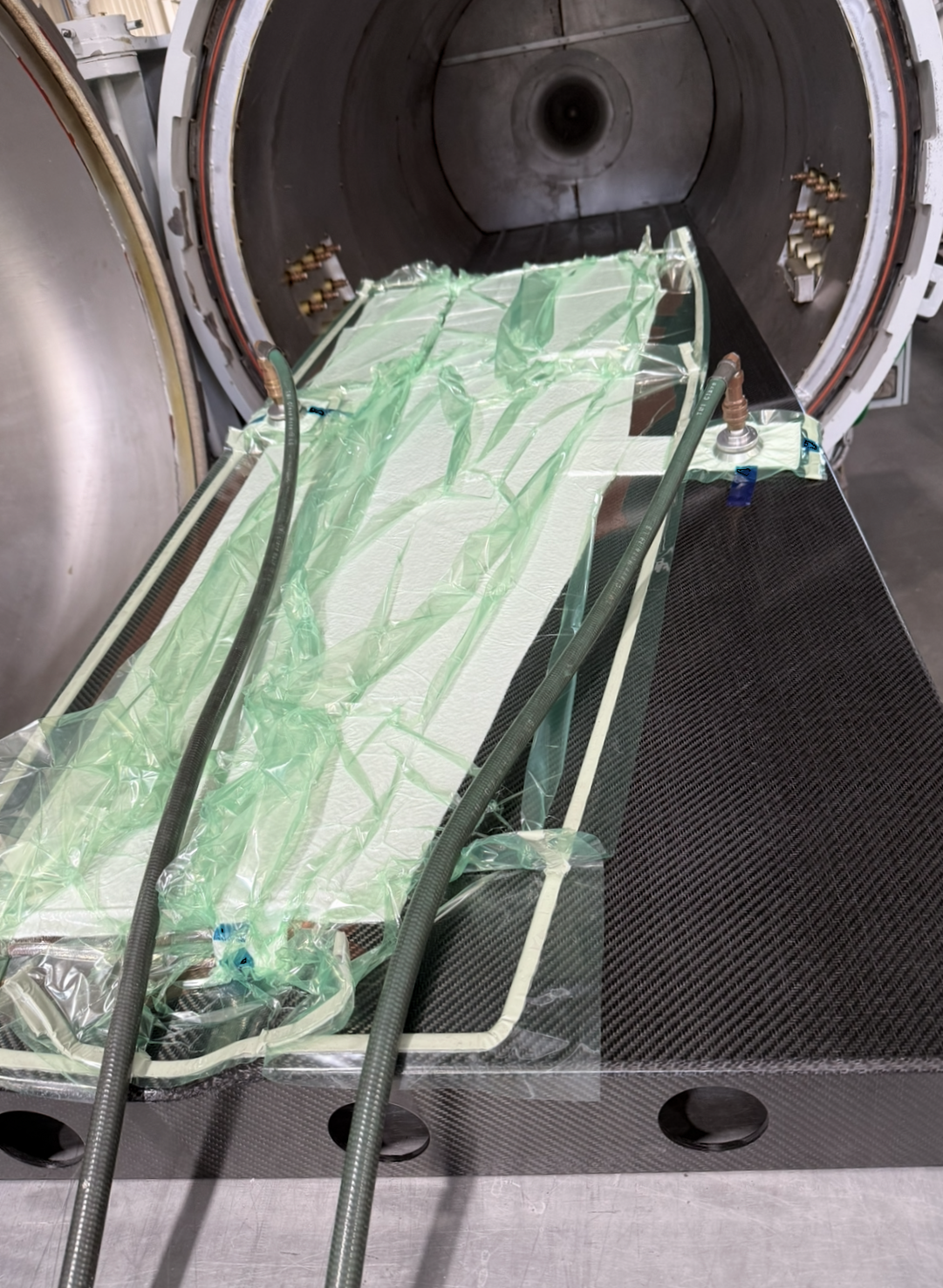 Close-up view of a spacecraft heat shield being tested or assembled, with carbon fiber panels, tubing, and protective plastic covering, inside a vacuum or testing chamber.