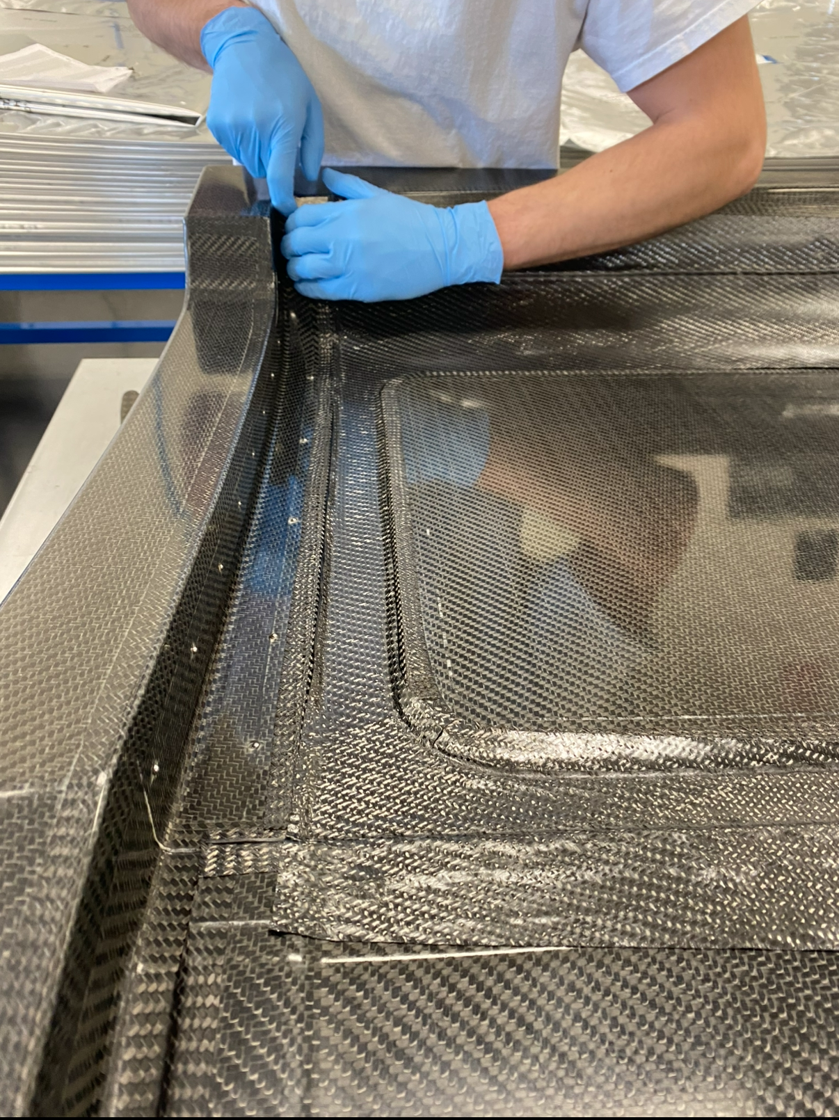 Person wearing blue gloves working on a carbon fiber car part.