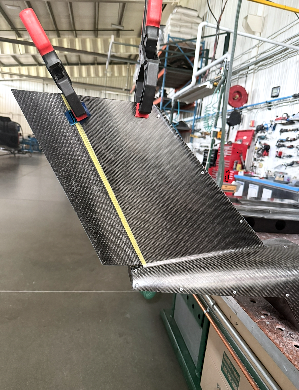A carbon fiber car part being glued or assembled with clamps in a workshop.