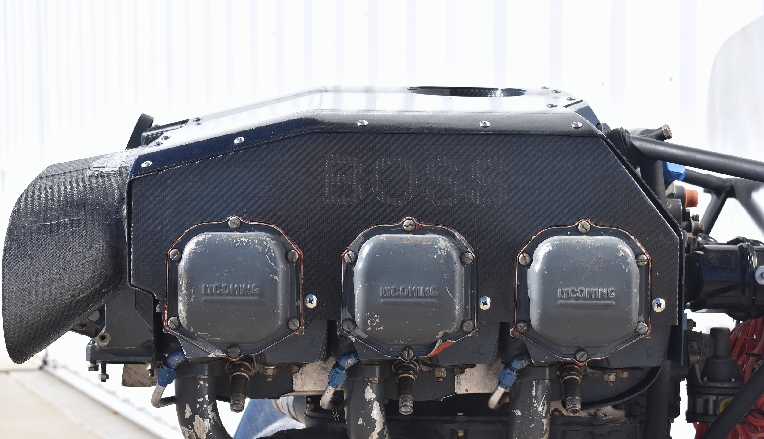 Close-up of a race car engine with three Lycoming components, a black carbon fiber cover with 
